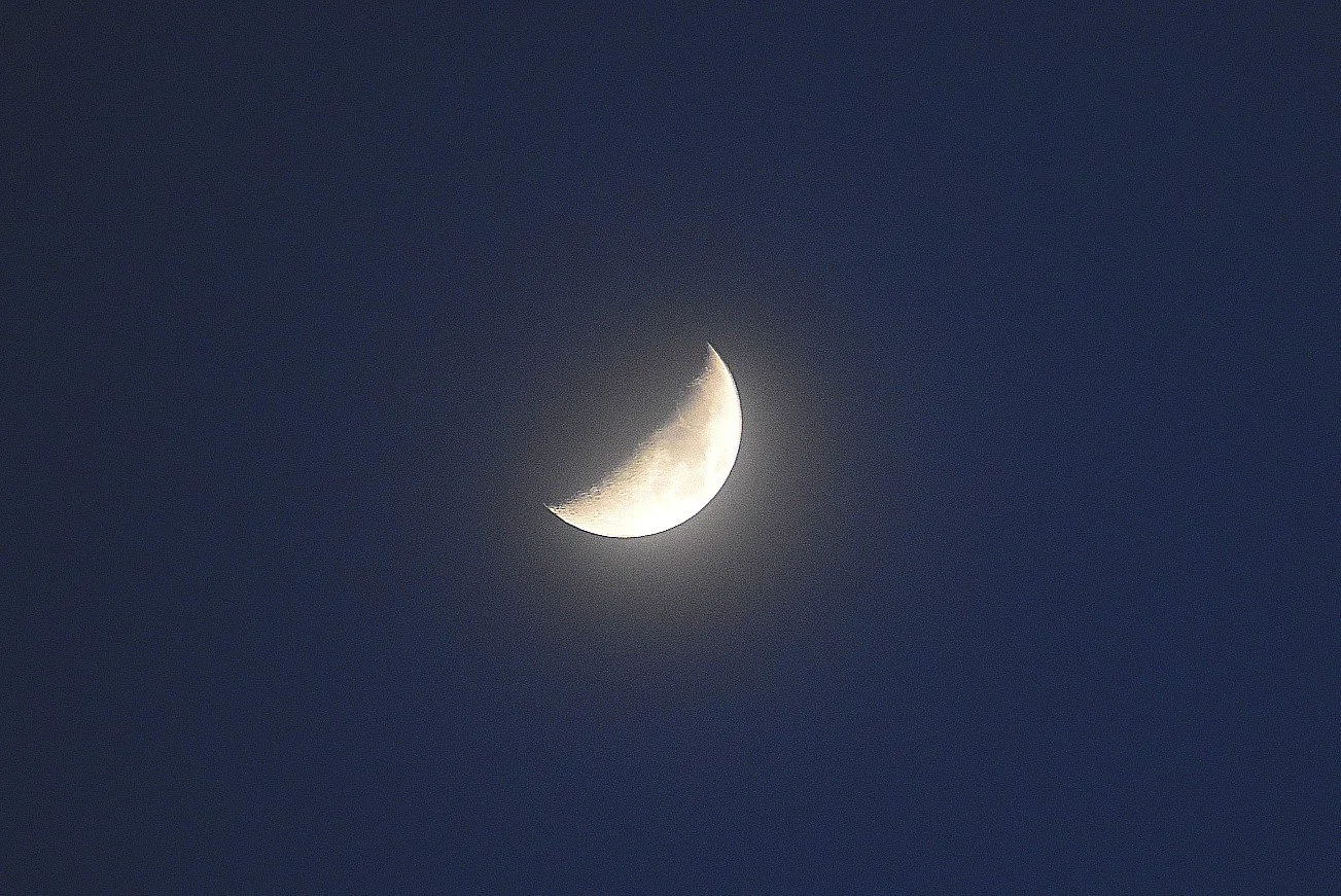 A crescent moon in a dark sky with minimal clouds.