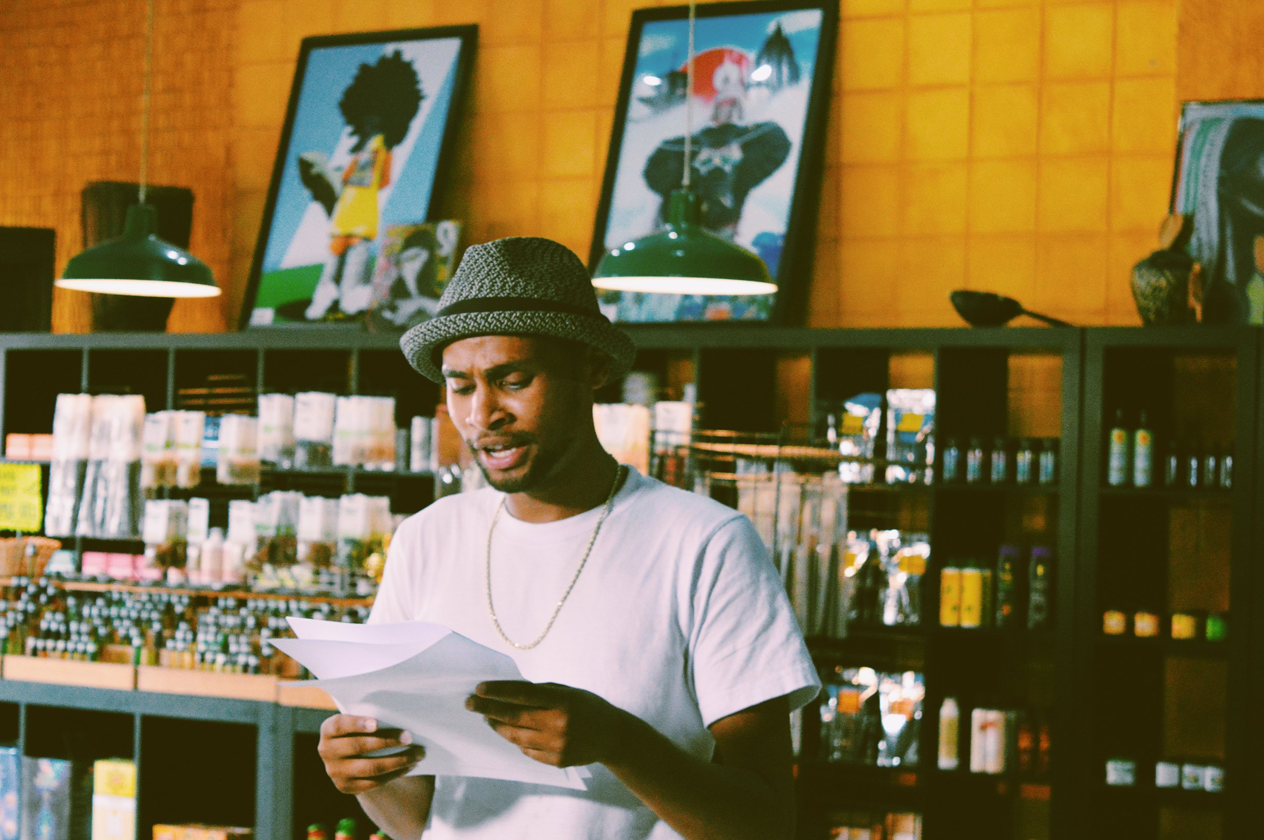 A man wearing a gray hat and white t-shirt looking at papers inside a store with wooden walls, black shelving, and colorful artwork on the wall.