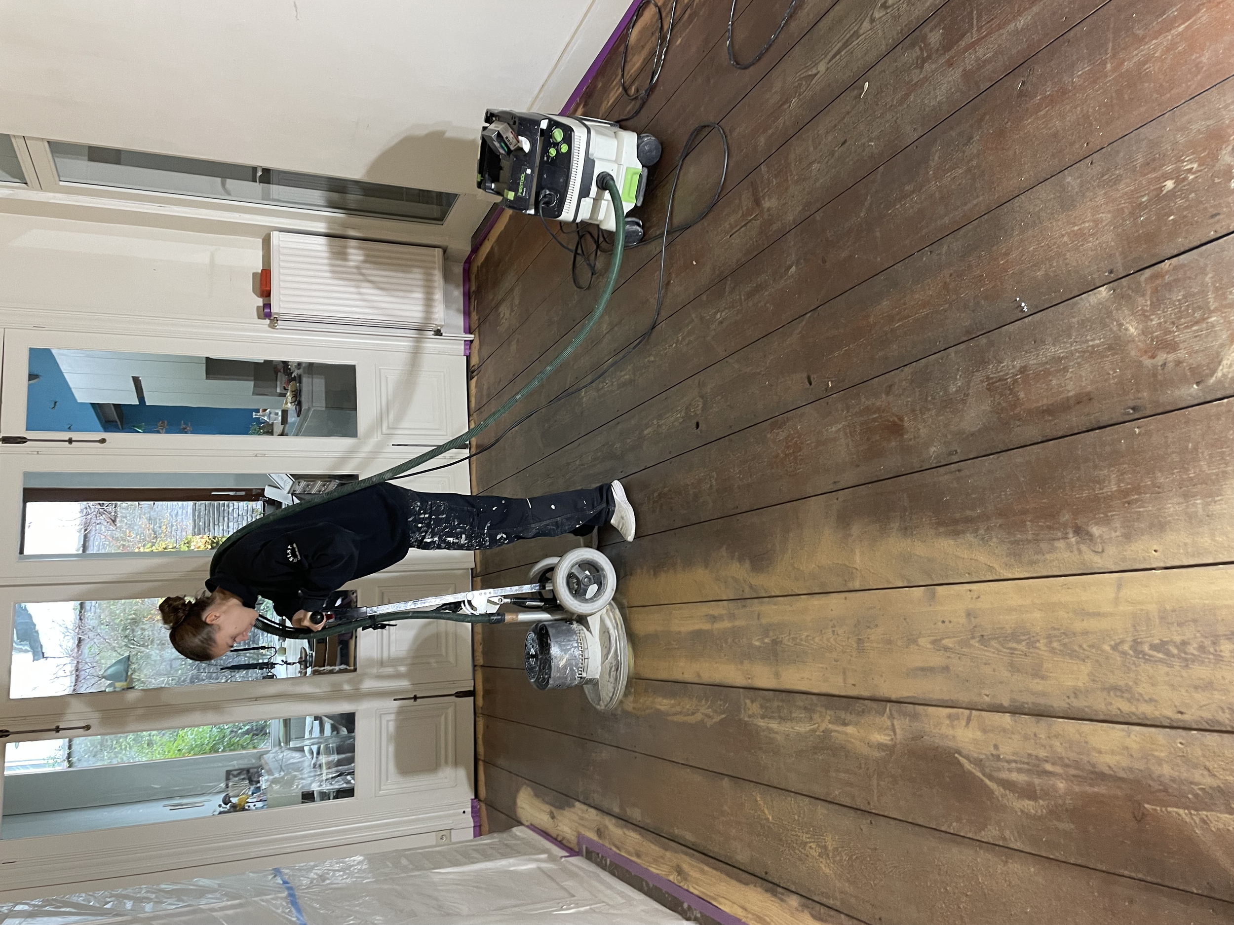 Het schuren van de houten vloer wordt gedaan met de Bona Schuurmachine