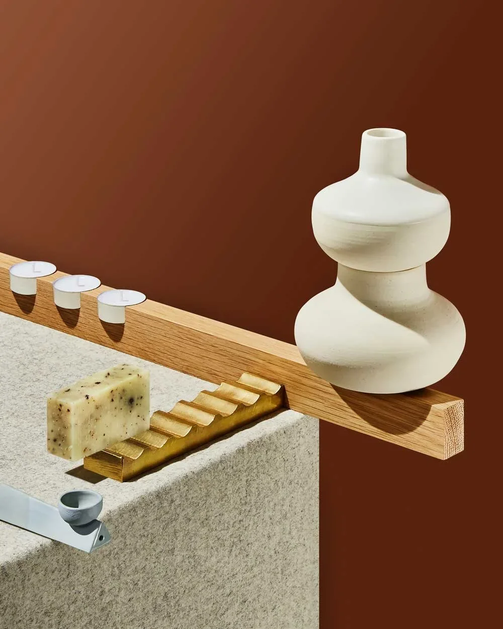 Decorative arrangement with candles, a soap bar, and a ceramic sculpture on a wooden ledge against a brown background.