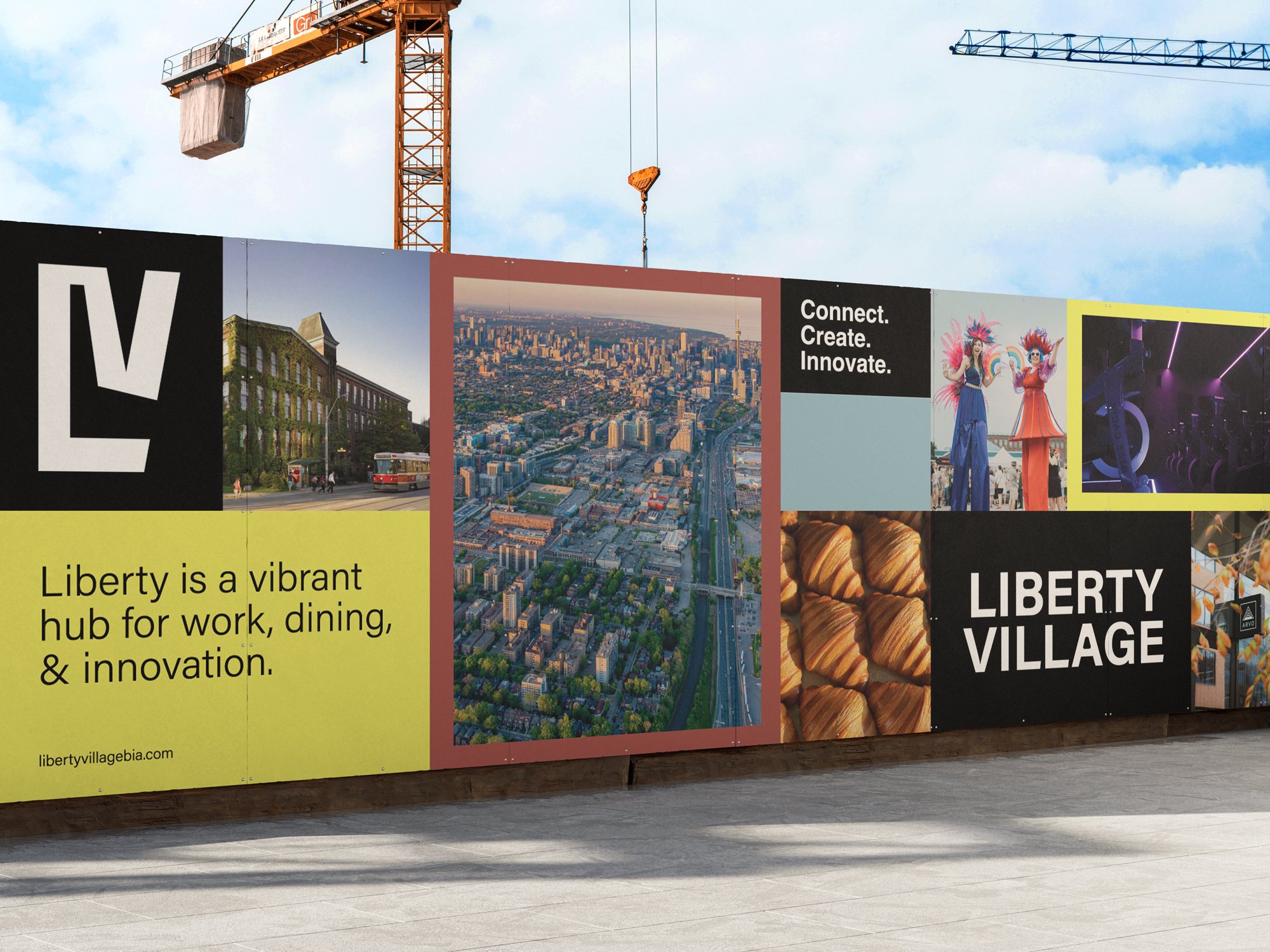 A large colorful billboard at Liberty Village displaying images and text, including aerial views of a city, performers in costumes, and a gym scene, with a construction crane visible in the background and a clear blue sky.