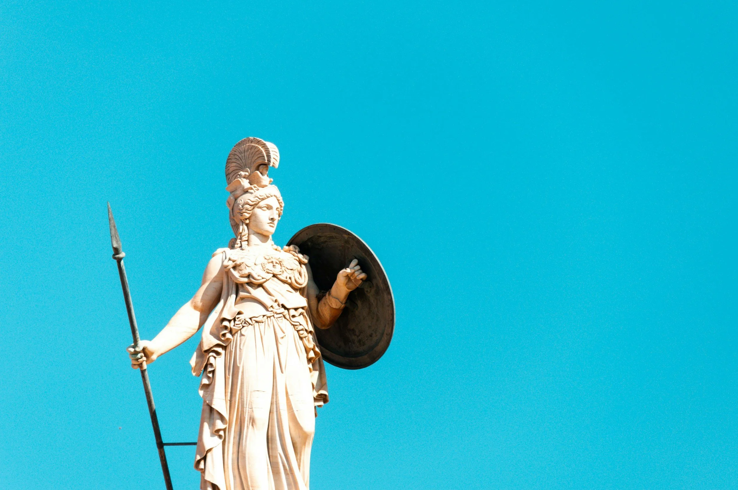 Statue of a woman dressed as a warrior holding a spear and shield against a clear blue sky.