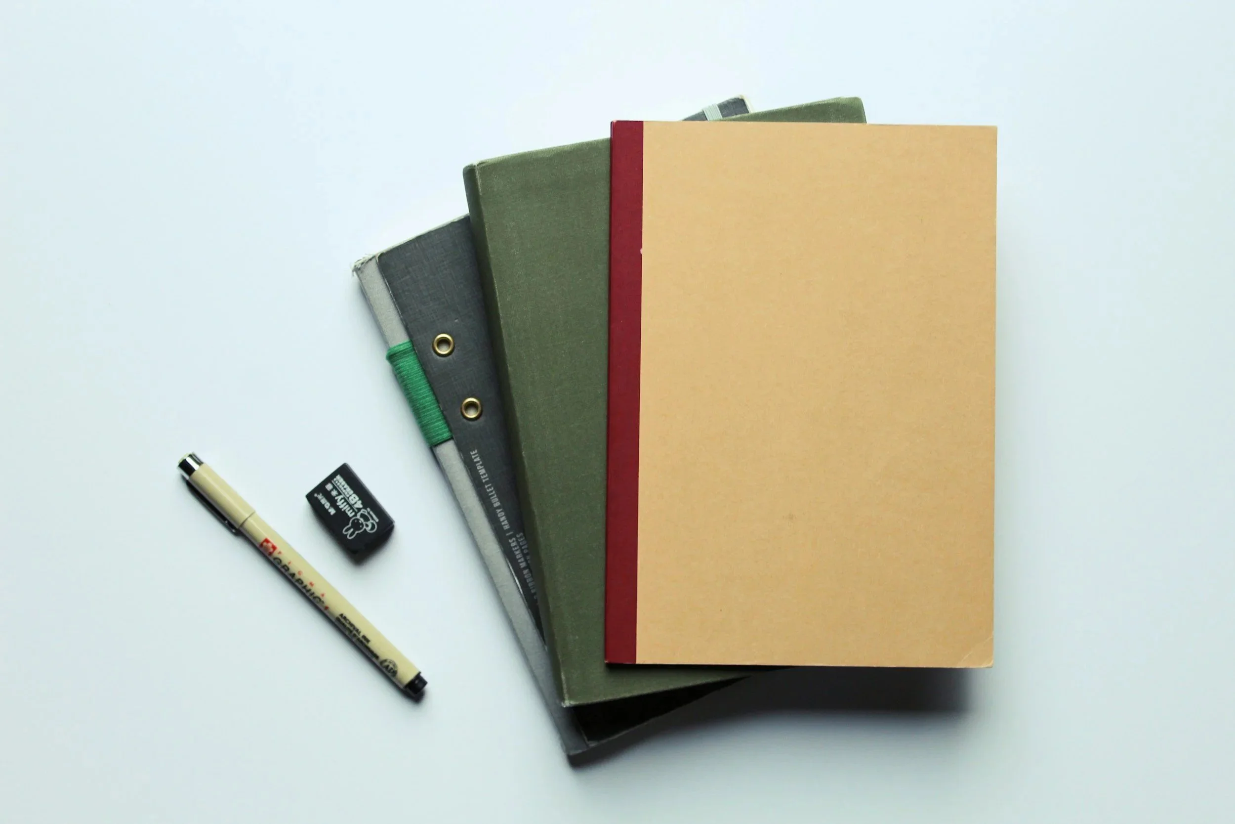 Stack of three hardcover books, a black and beige marker, and a black eraser on a white surface.