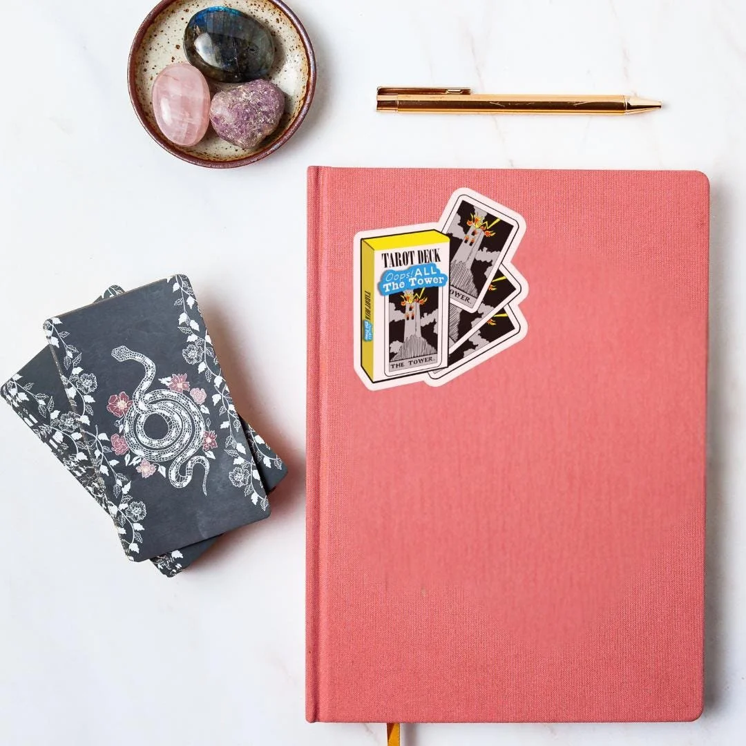 oops all towers sticker on a spiritual journal with some tarot cards and a crystal