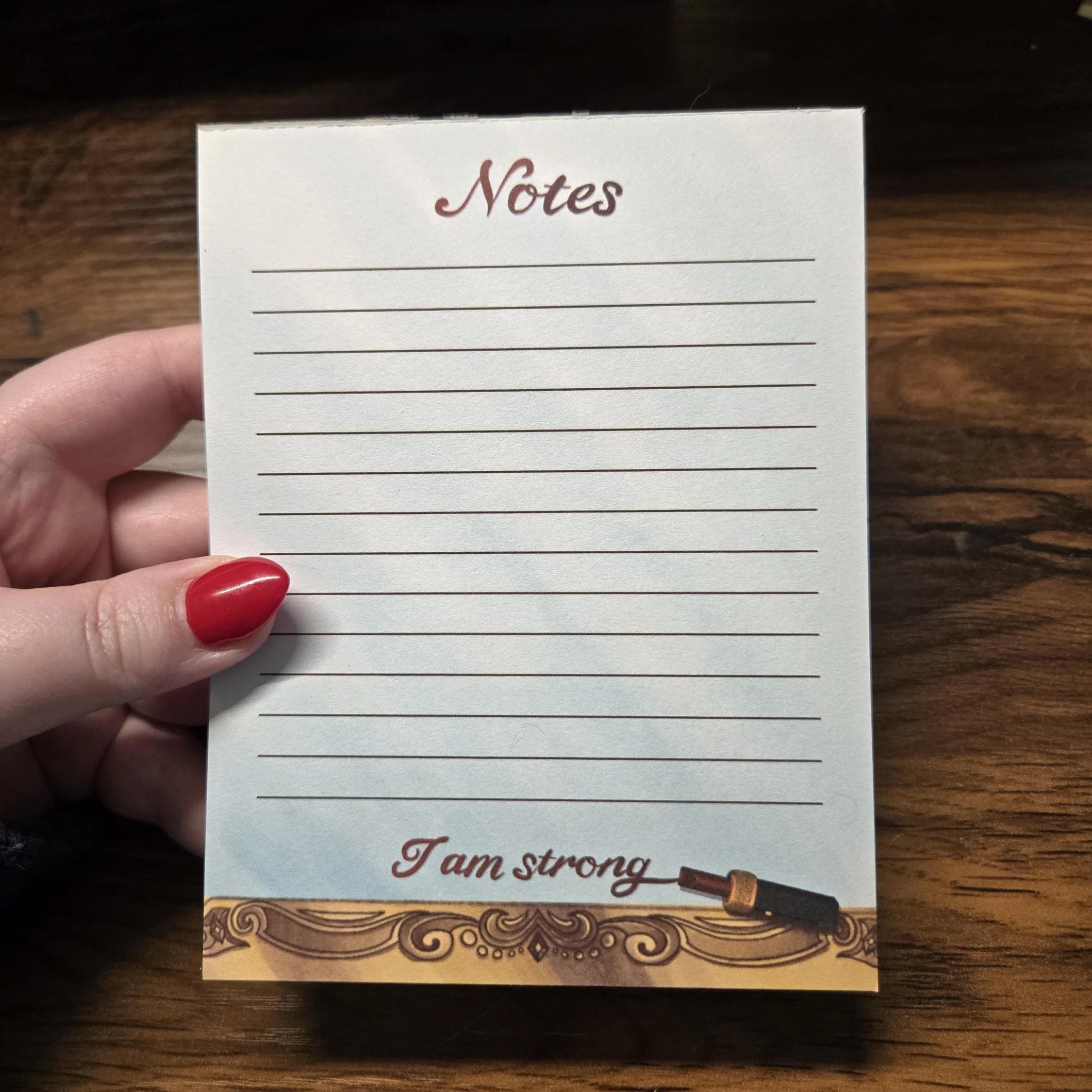notepad that looks like a mirror with the bottom of the frame being gold with flourishes and vintage lipstick drawn on the mirror that says I am strong
