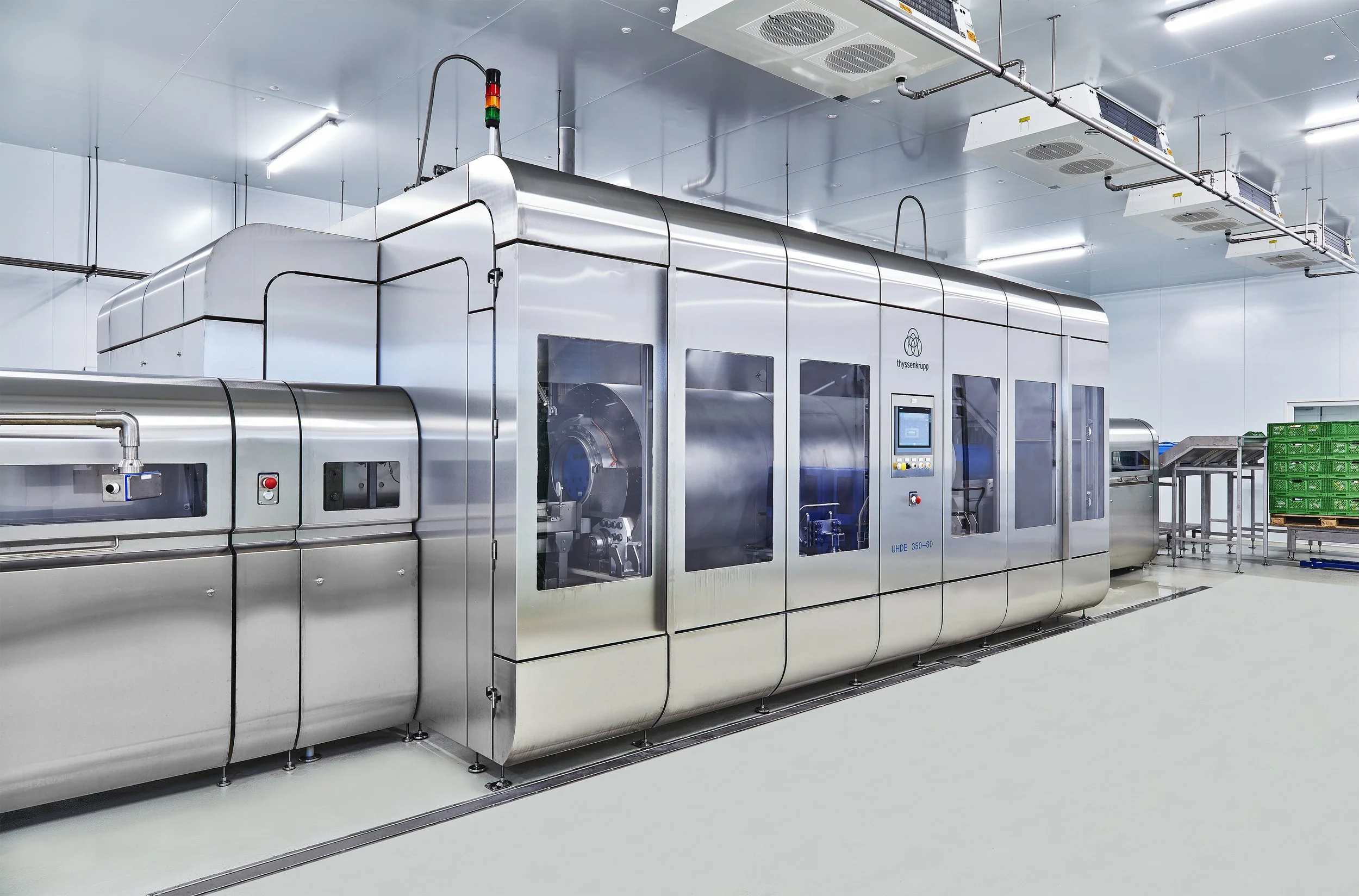 A large, stainless steel HPP machine inside a clean, modern manufacturing facility, with control panels and transparent windows.