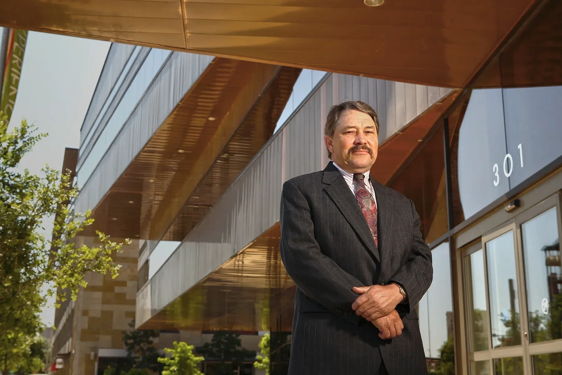 Professional executive portrait photographed outside a modern corporate office, emphasizing leadership, confidence, and architectural context.