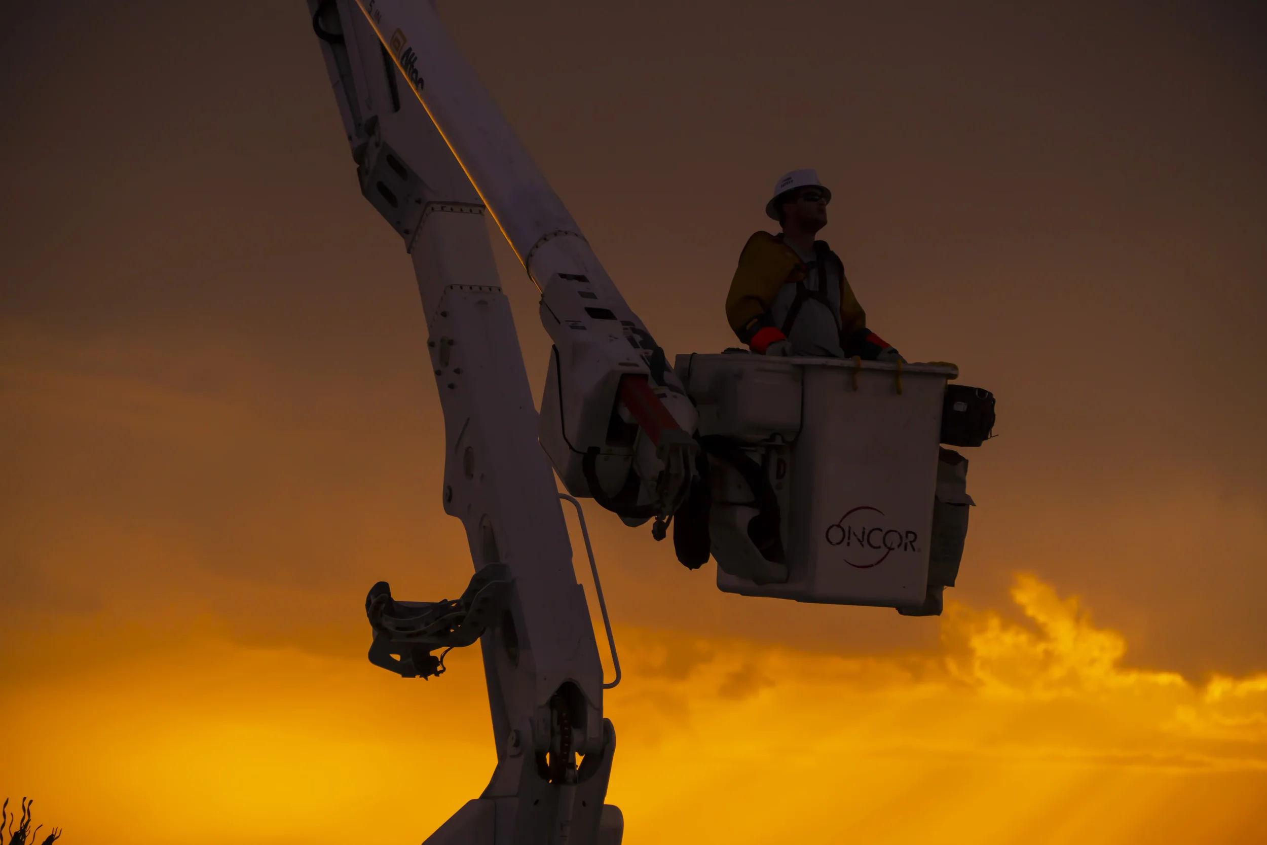 Dallas industrial photography featuring a utility technician operating from a bucket truck at sunset, highlighting power line maintenance, elevated work safety, and essential electrical infrastructure.