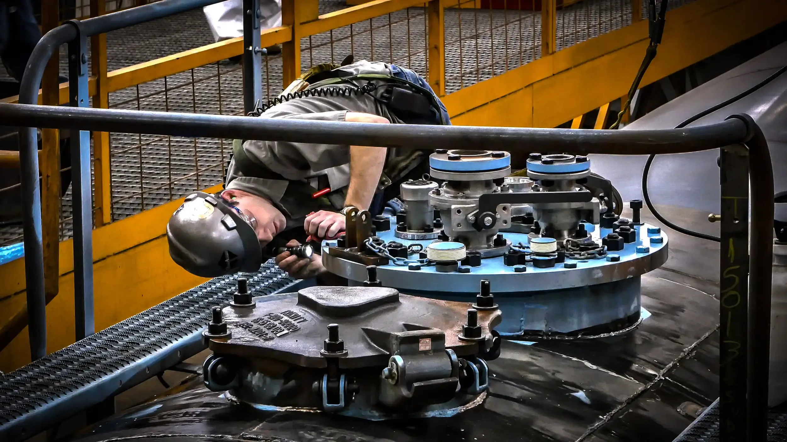 Industrial photography in Dallas showing a technician inspecting mechanical components on a large storage tank, emphasizing maintenance procedures, precision inspection, and operational safety in industrial facilities.