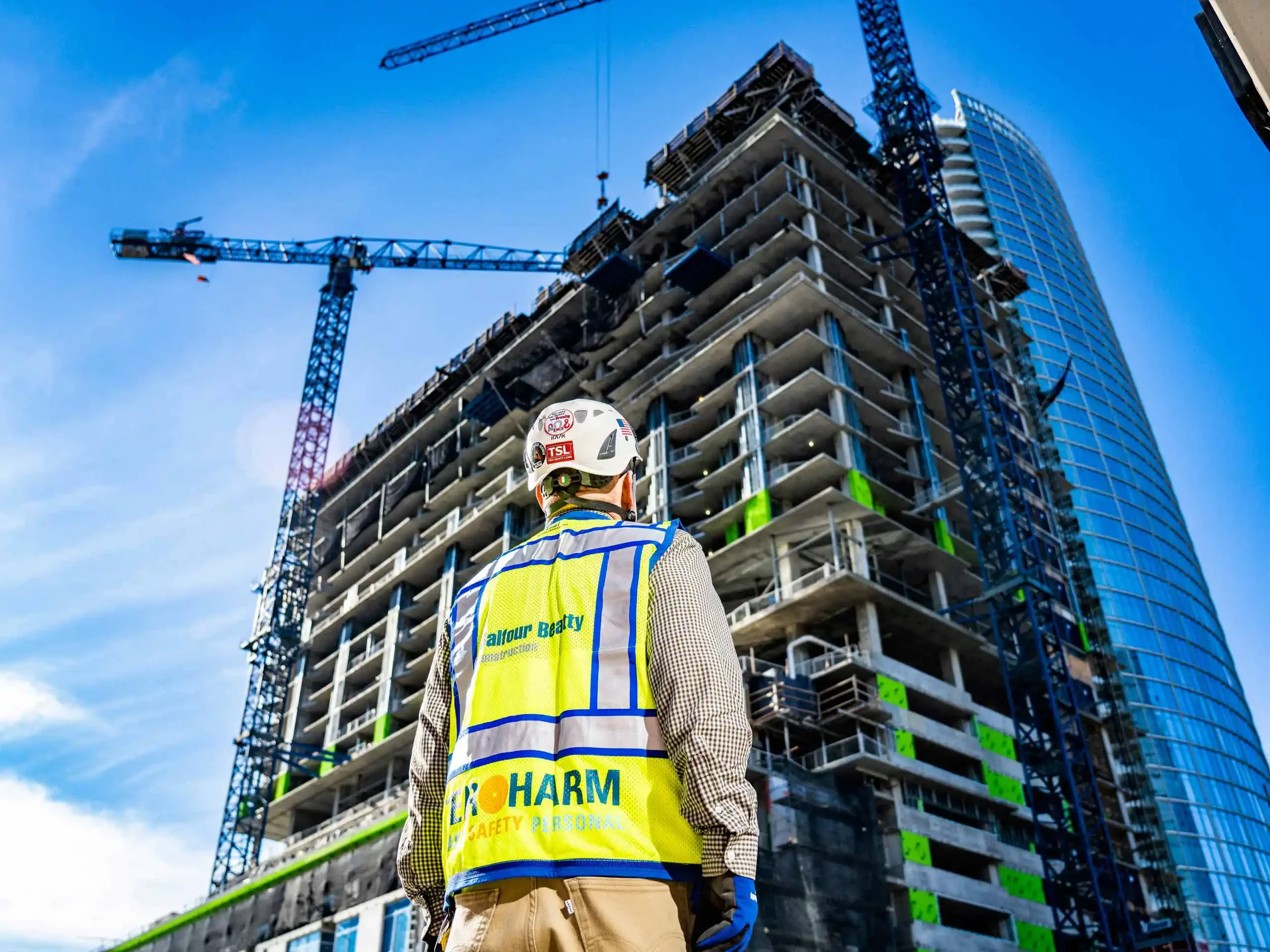 Dallas industrial construction photography showing a safety-certified professional overseeing a high-rise building project with tower cranes, documenting large-scale commercial construction, workforce safety, and project progress for corporate market