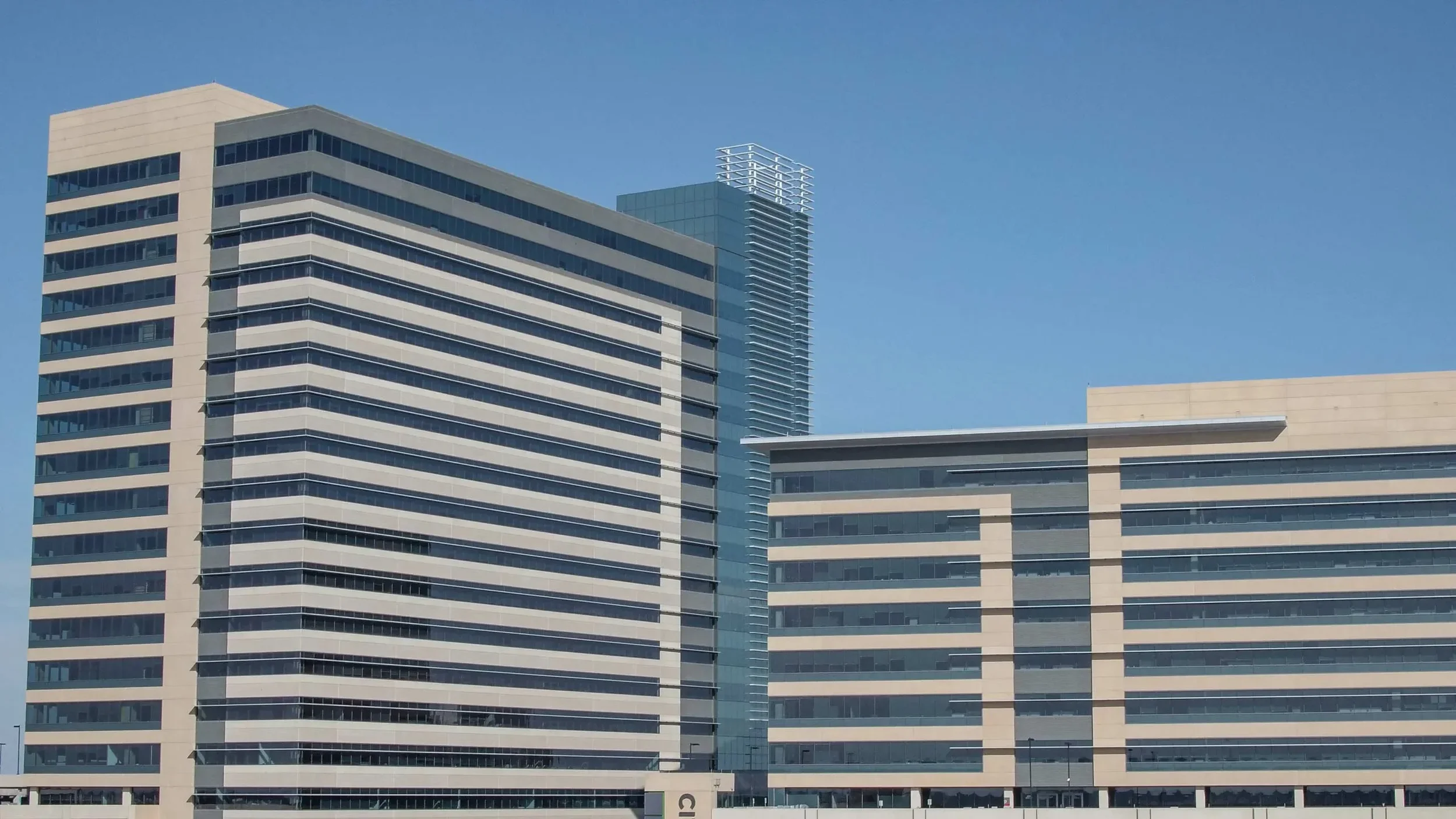 Drone aerial view of a modern commercial office complex in Dallas showcasing clean architectural lines, glass façades, and surrounding urban development under clear blue skies.