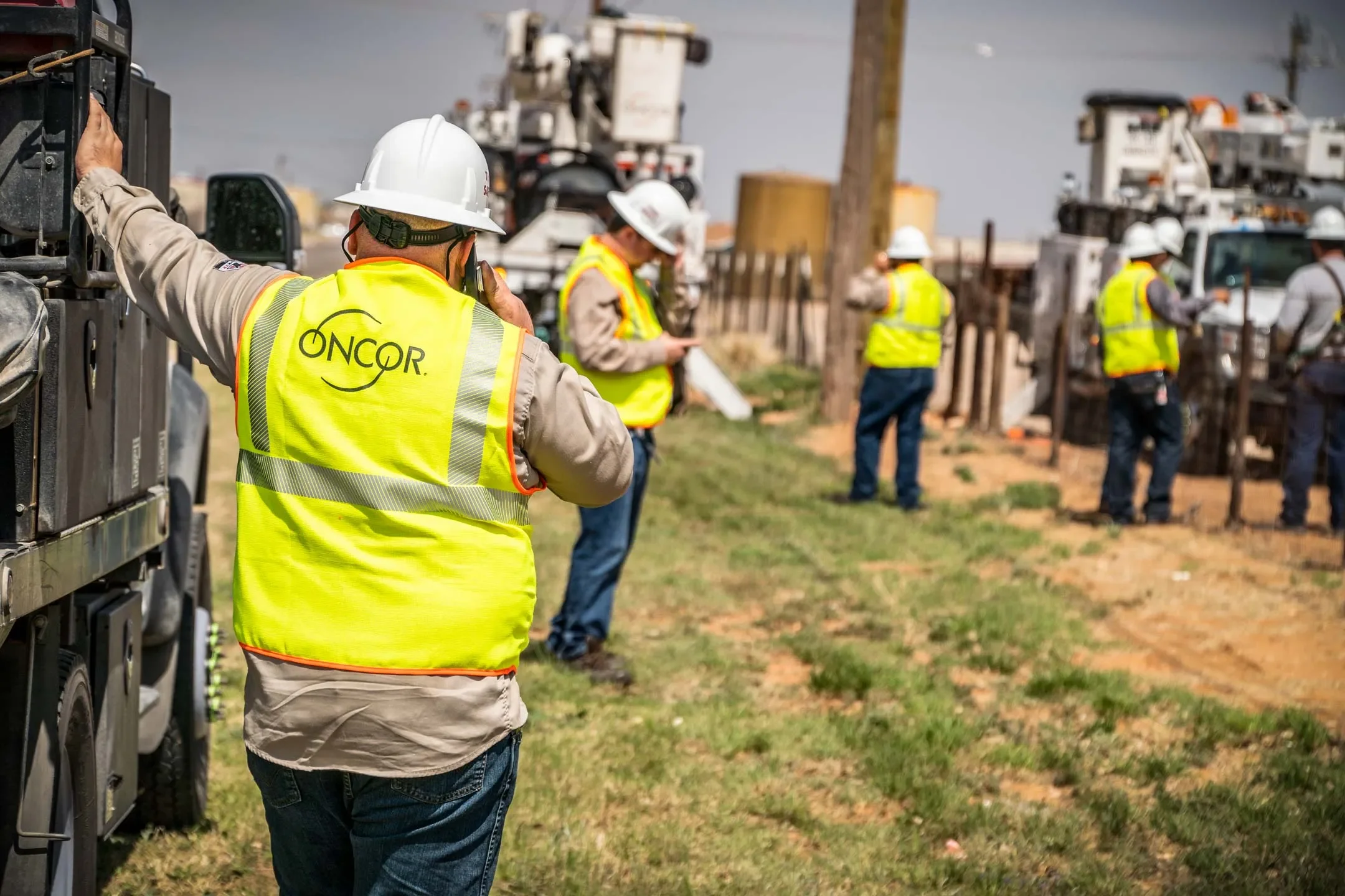 Industrial utility photography in Dallas capturing an Oncor field crew coordinating power infrastructure work on an active job site, emphasizing teamwork, communication, and critical electrical service operations.