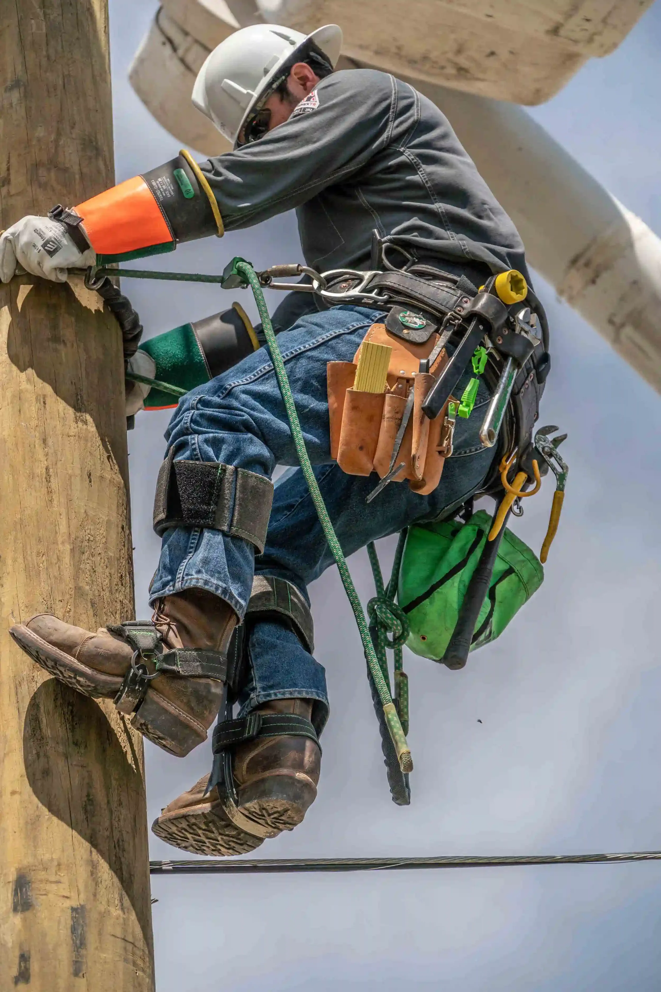 Dallas industrial utility photography capturing an electrical line worker climbing a utility pole using safety harnesses and protective gear, showcasing power infrastructure maintenance, skilled labor, and workplace safety.
