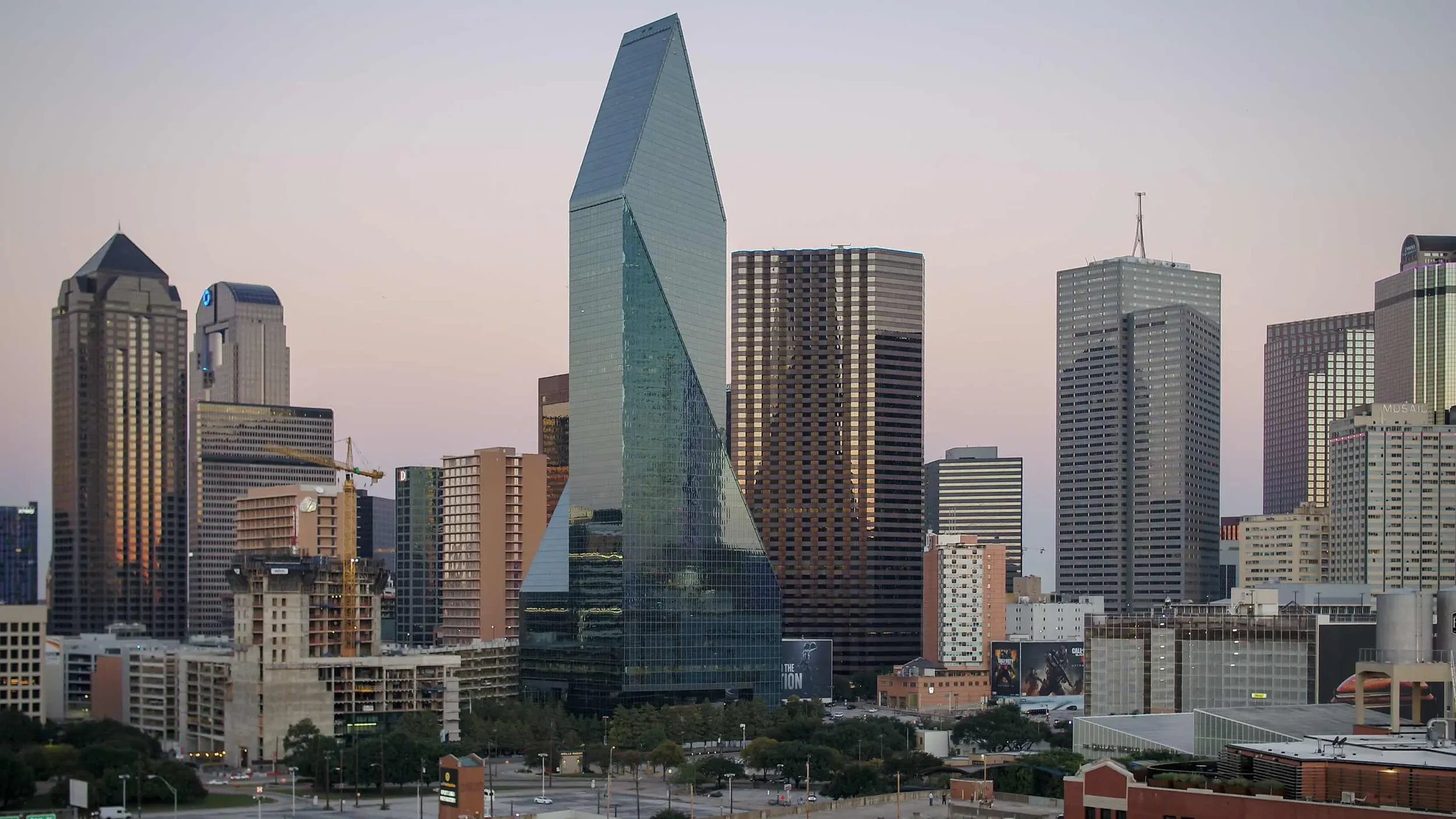 Aerial drone image of the Dallas skyline featuring iconic modern skyscrapers and urban density, captured during early evening with soft ambient light.