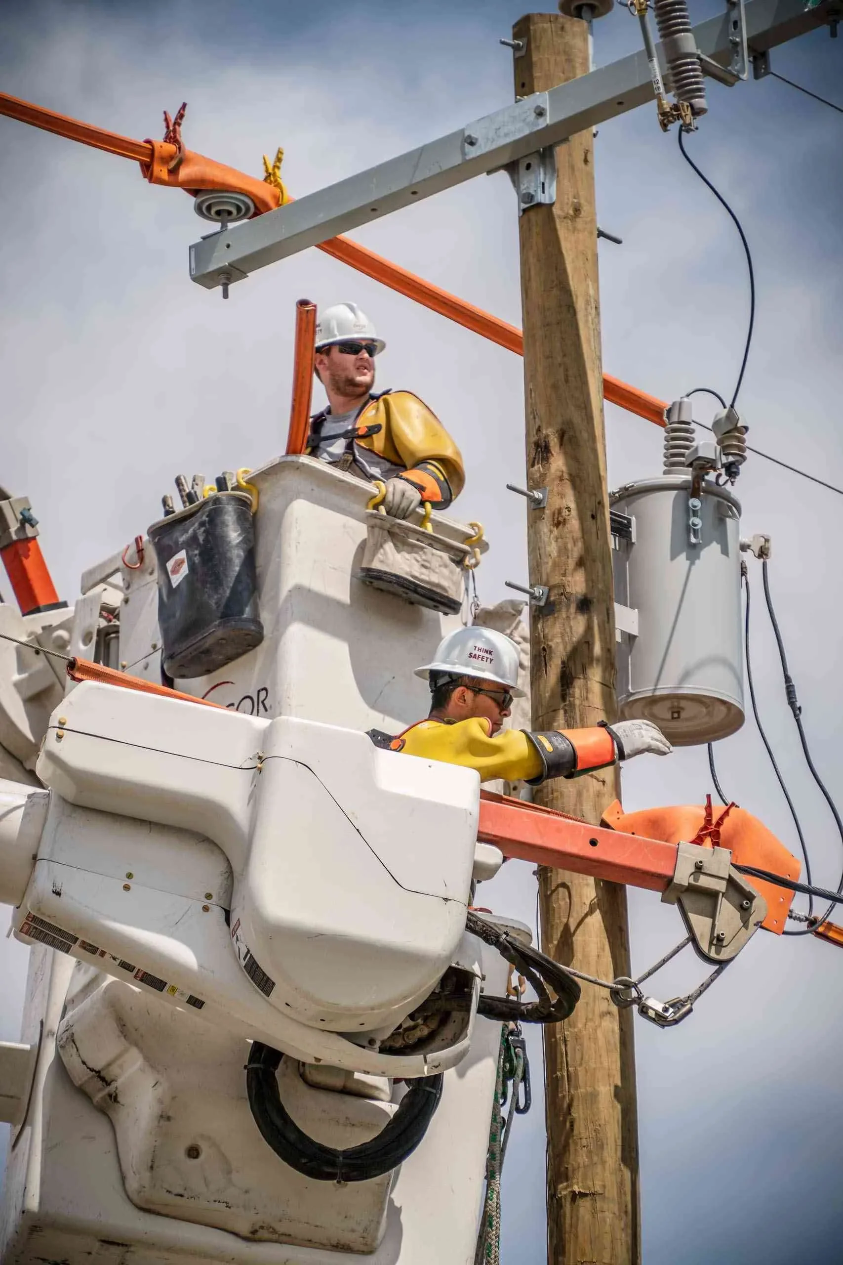 Dallas industrial utility photography featuring electrical line workers performing elevated maintenance from a bucket truck, highlighting power infrastructure, safety procedures, and critical utility operations.