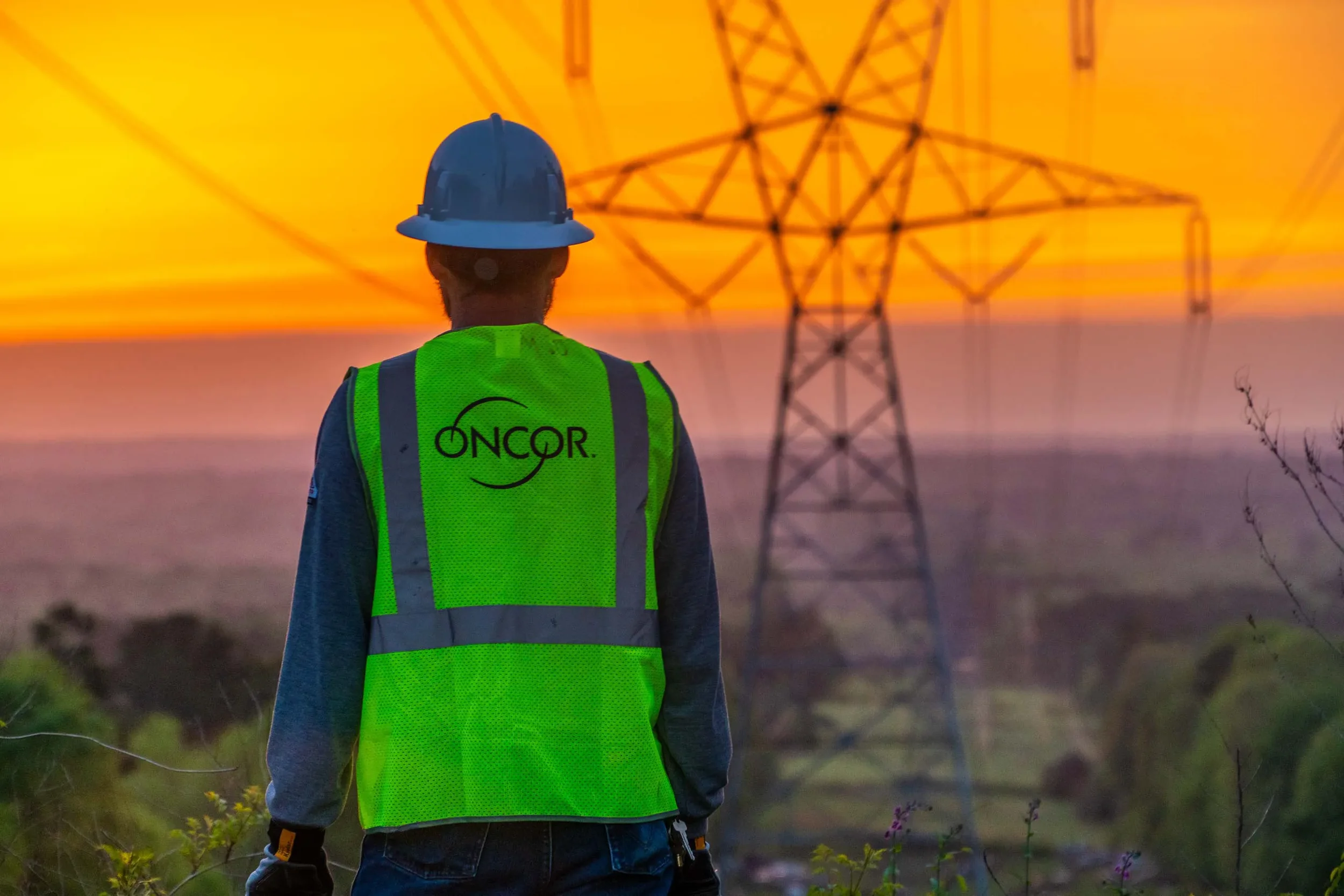 Industrial photography in Texas showing a utility worker overseeing high-voltage power transmission lines at sunset, highlighting electrical infrastructure, grid reliability, and large-scale energy operations.