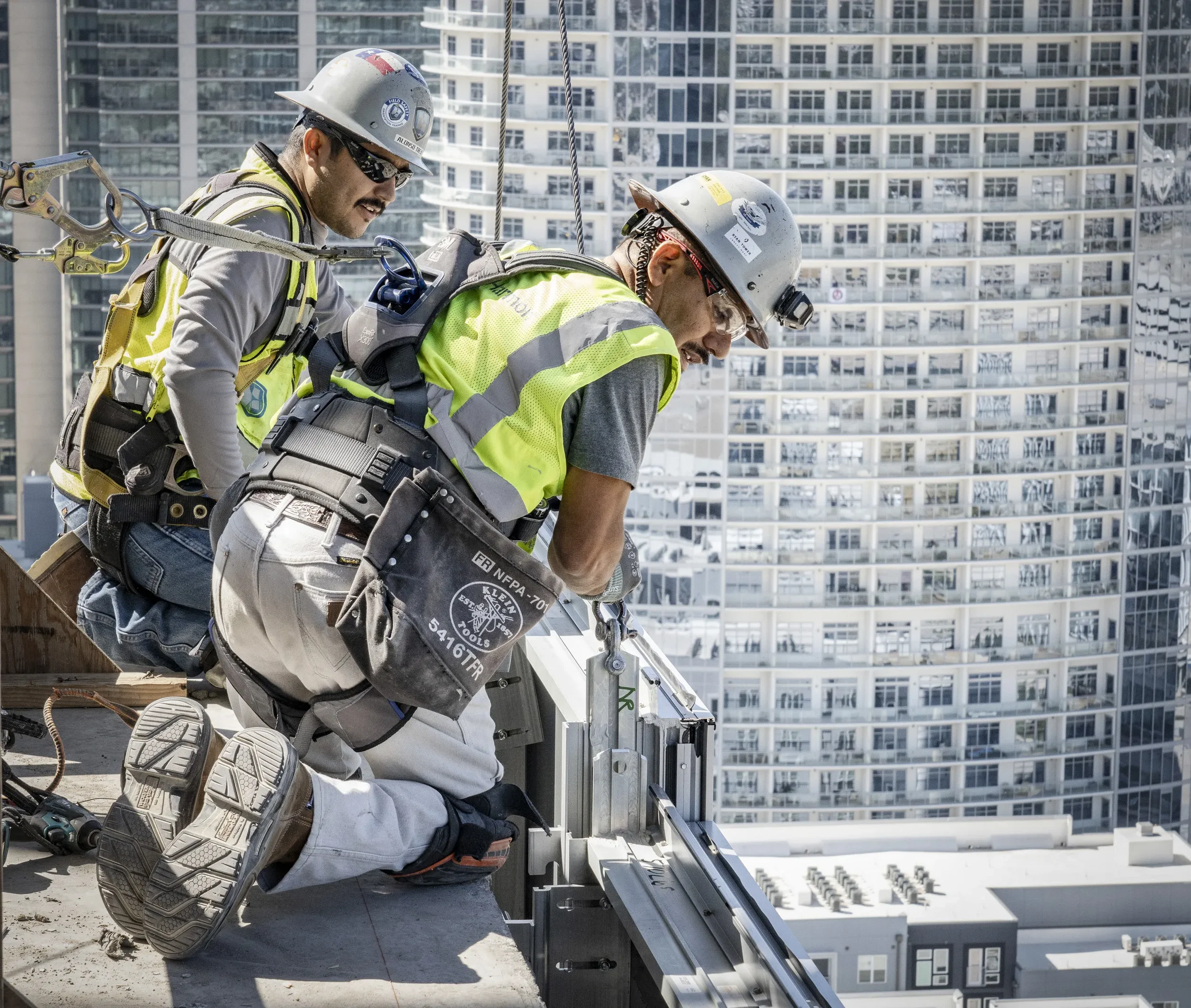 Dallas industrial construction photography featuring skilled workers installing building components at height, emphasizing jobsite safety, precision installation, and large-scale urban construction.