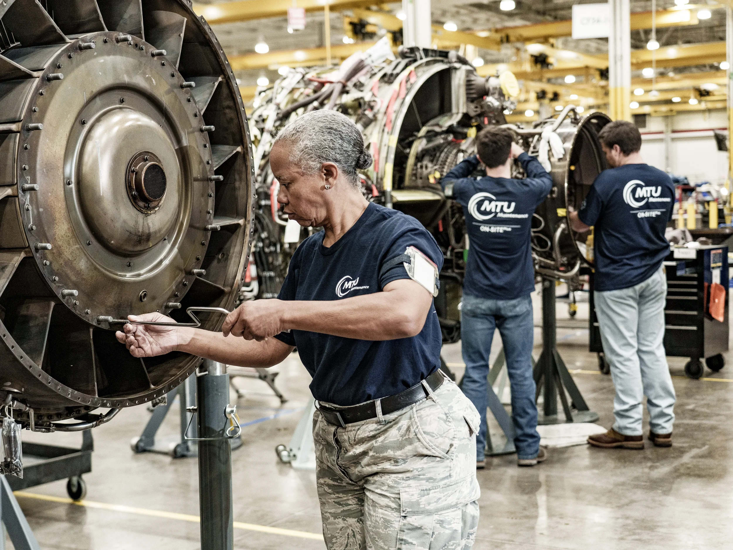 Dallas industrial manufacturing photography showing technicians inspecting turbine components in an aviation maintenance environment, emphasizing quality control, teamwork, and complex mechanical systems.