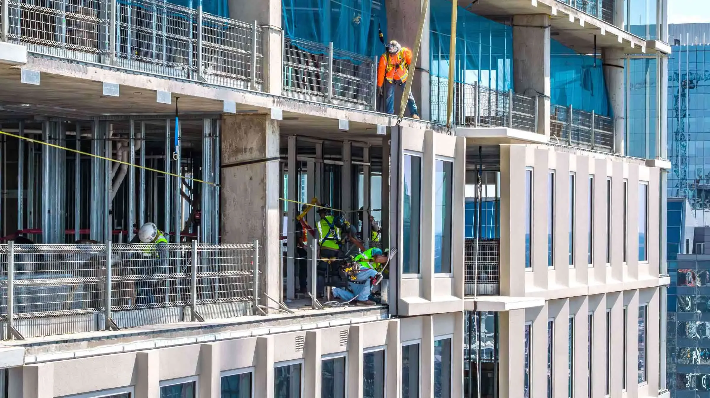 Aerial drone photograph capturing construction crews installing exterior facade panels on a high-rise building in Dallas, highlighting active commercial construction, safety practices, and large-scale urban development.