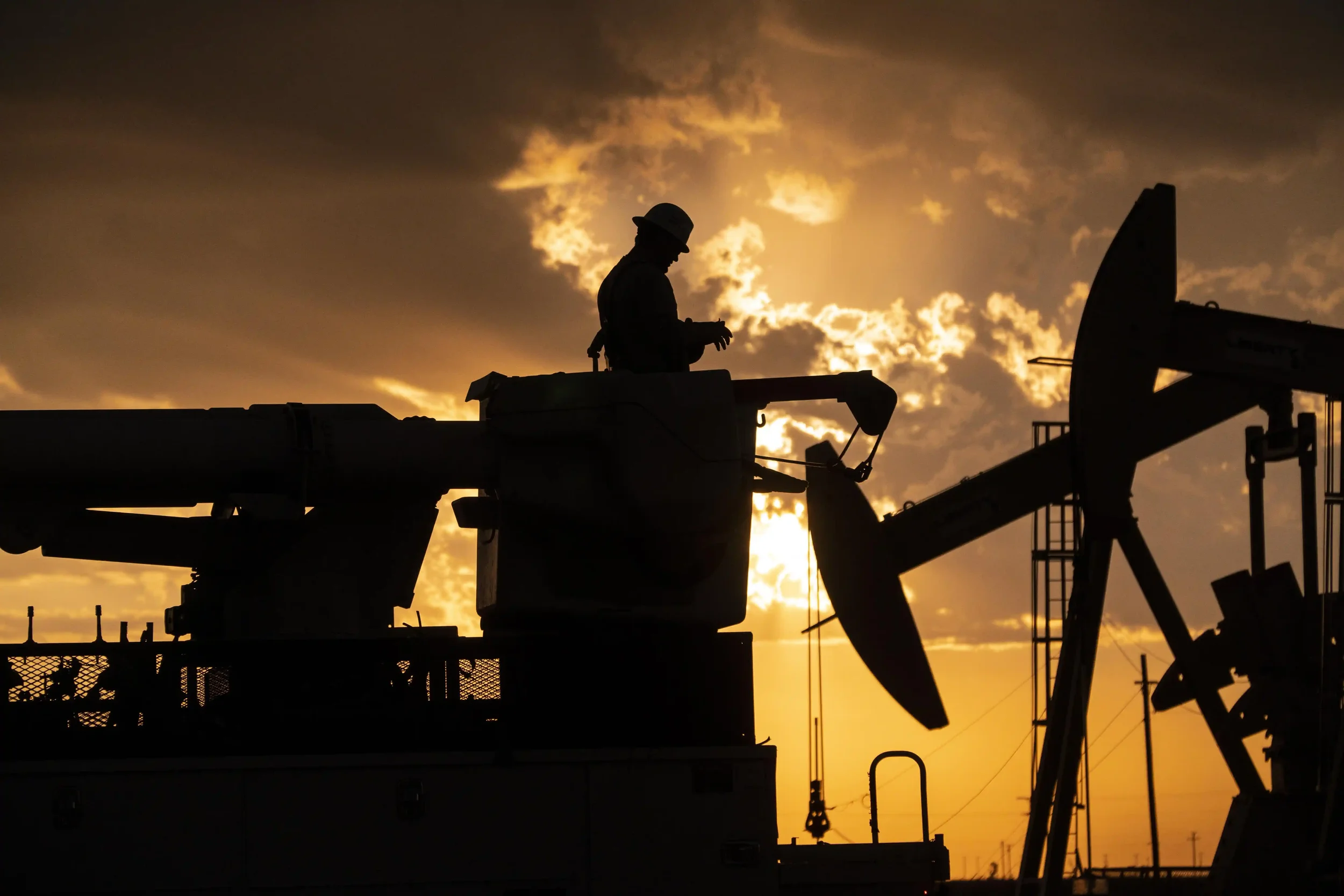 Dallas industrial energy photography featuring an oilfield worker silhouetted against the sky beside active pumpjacks, illustrating oil and gas production, energy infrastructure, and field operations.