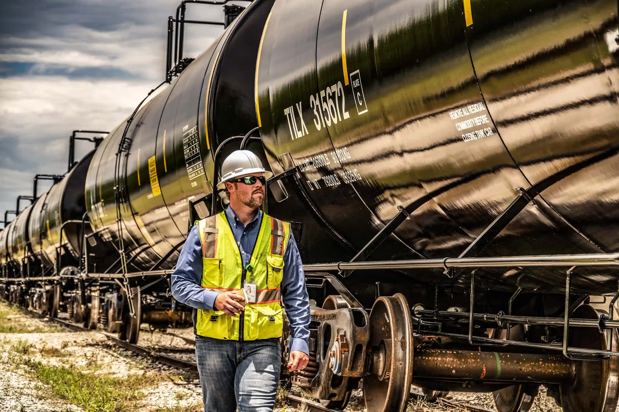 Rail operations specialist conducts a safety walkthrough alongside loaded tanker railcars at an active rail facility, emphasizing hazardous materials handling, transportation compliance, and industrial freight logistics.

Why this change