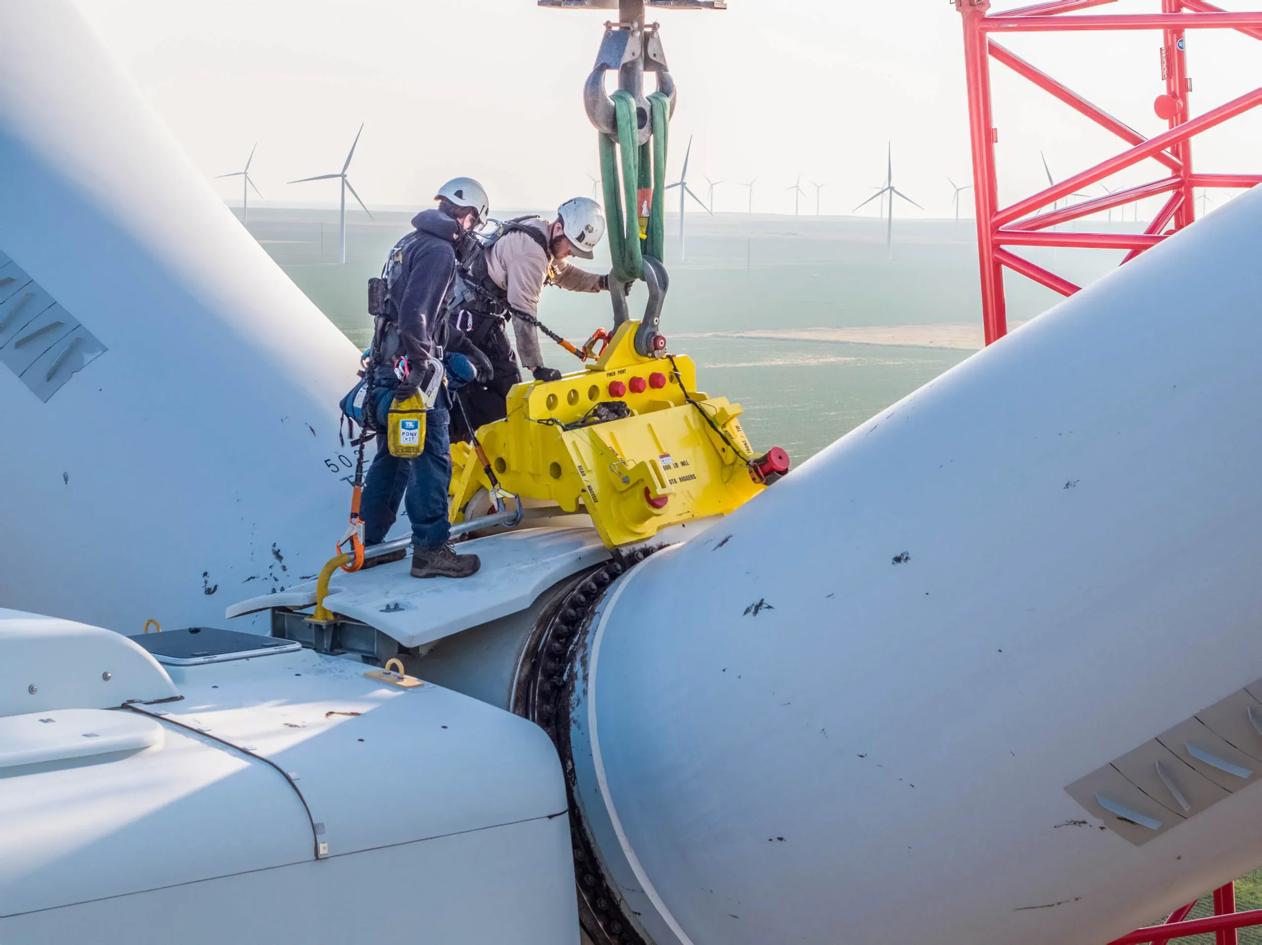 FAA-certified drone photograph of wind turbine technicians performing maintenance at height, emphasizing industrial safety procedures, renewable energy infrastructure, and scale.