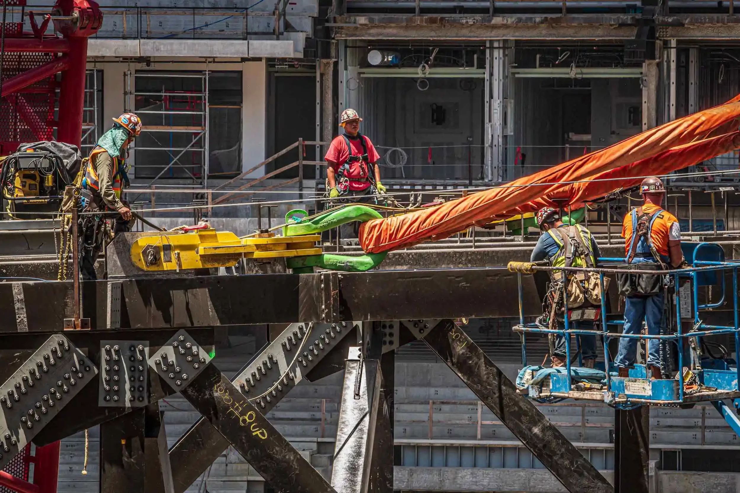 Dallas industrial construction photography capturing ironworkers coordinating heavy rigging operations on a major construction project, highlighting teamwork, structural steel installation, and complex industrial lifting processes.