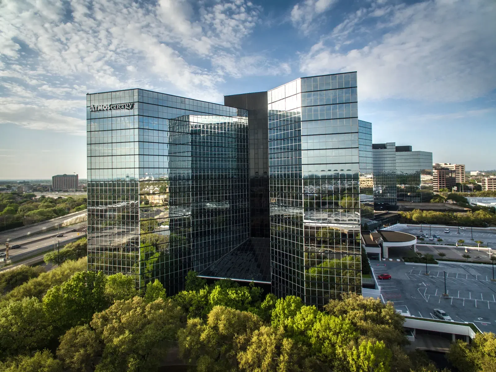 Aerial drone view of a modern glass corporate headquarters surrounded by mature landscaping, showcasing architectural symmetry and professional business environments in Dallas, Texas.

2. Highway Interchange at Sunset – Urban Infrastructure