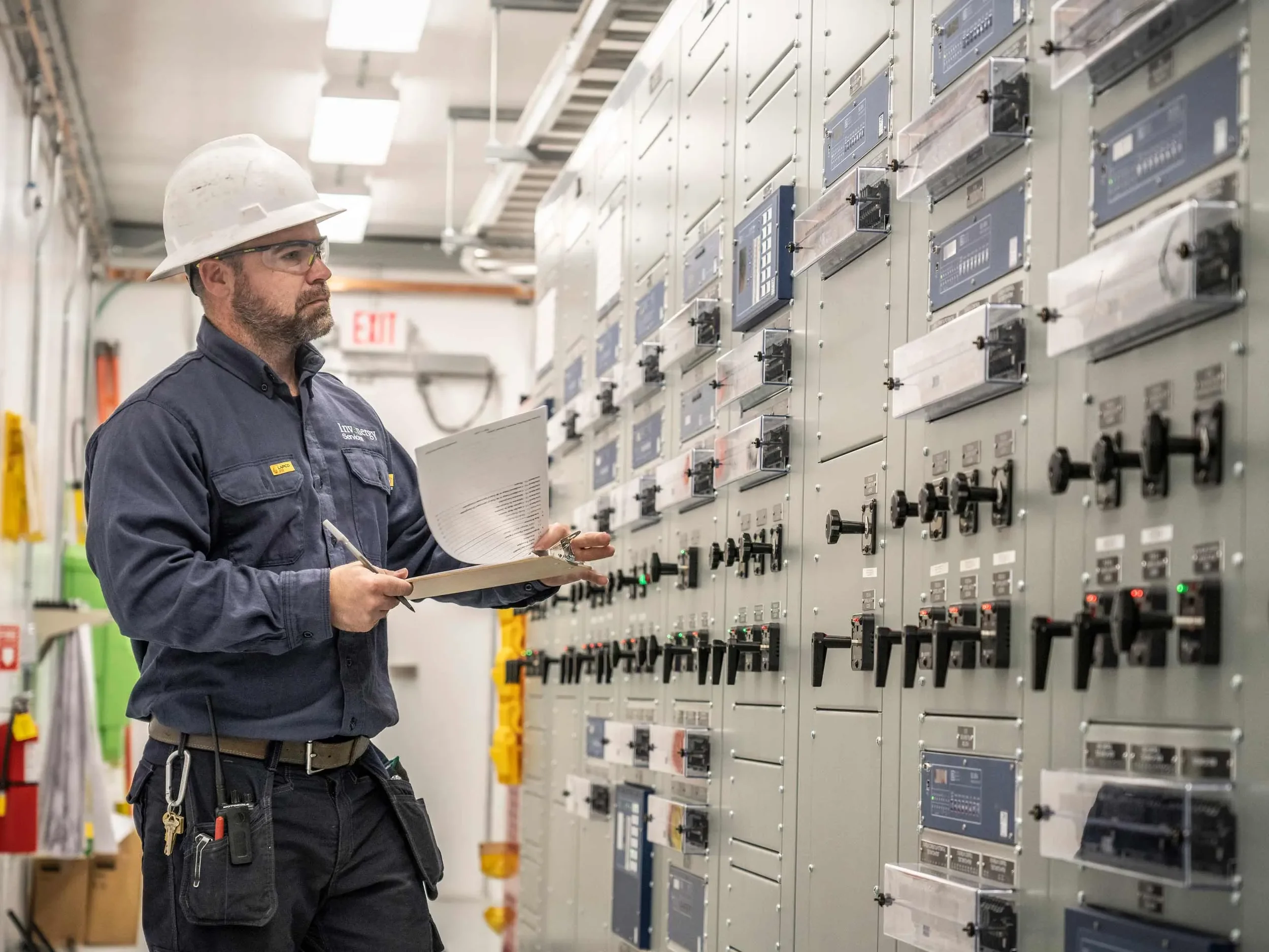 Electrical systems specialist reviews control panel data inside a power distribution facility, highlighting system monitoring, preventative maintenance, and utility infrastructure reliability.