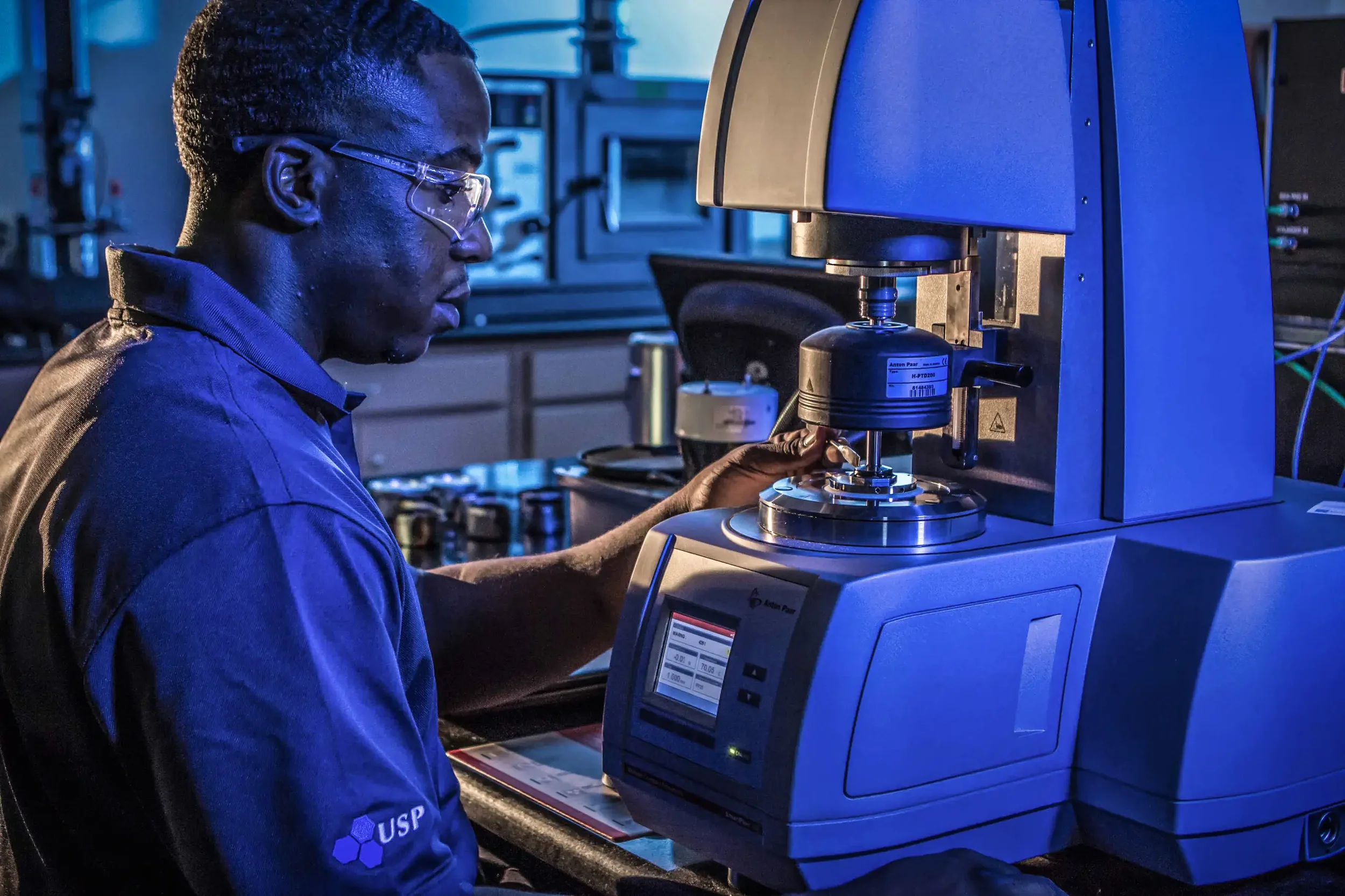 Industrial photography in Dallas featuring a technician operating advanced materials testing equipment in a controlled laboratory environment, emphasizing compliance testing, precision measurement, and industrial quality assurance.