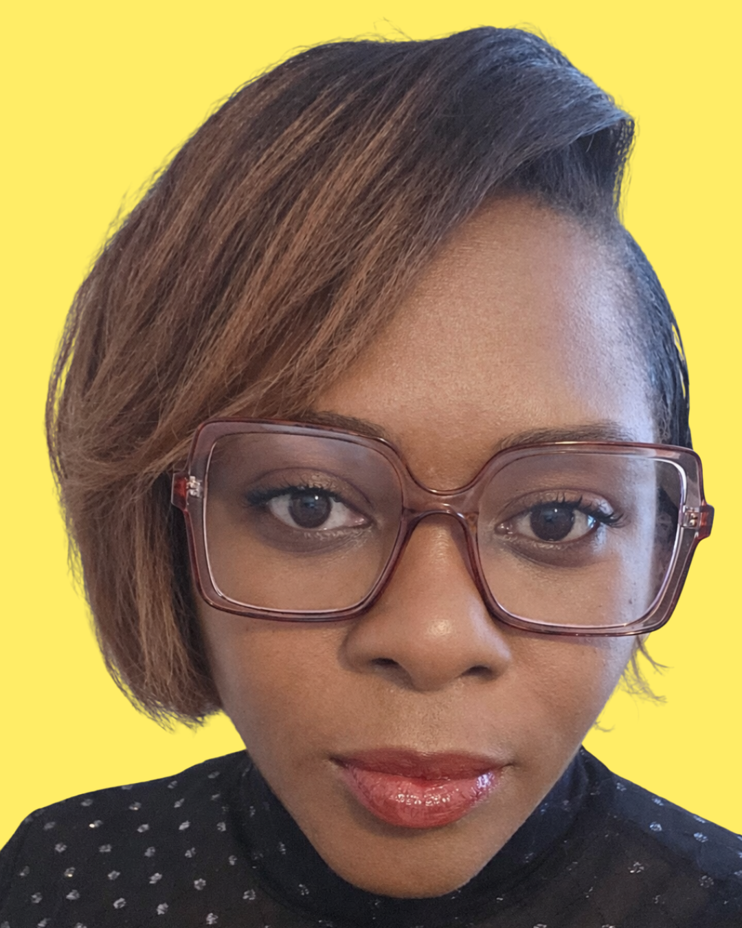 Close-up of a woman with short, brown hair wearing large pink glasses and a black top with small white polka dots, set against a bright yellow background.
