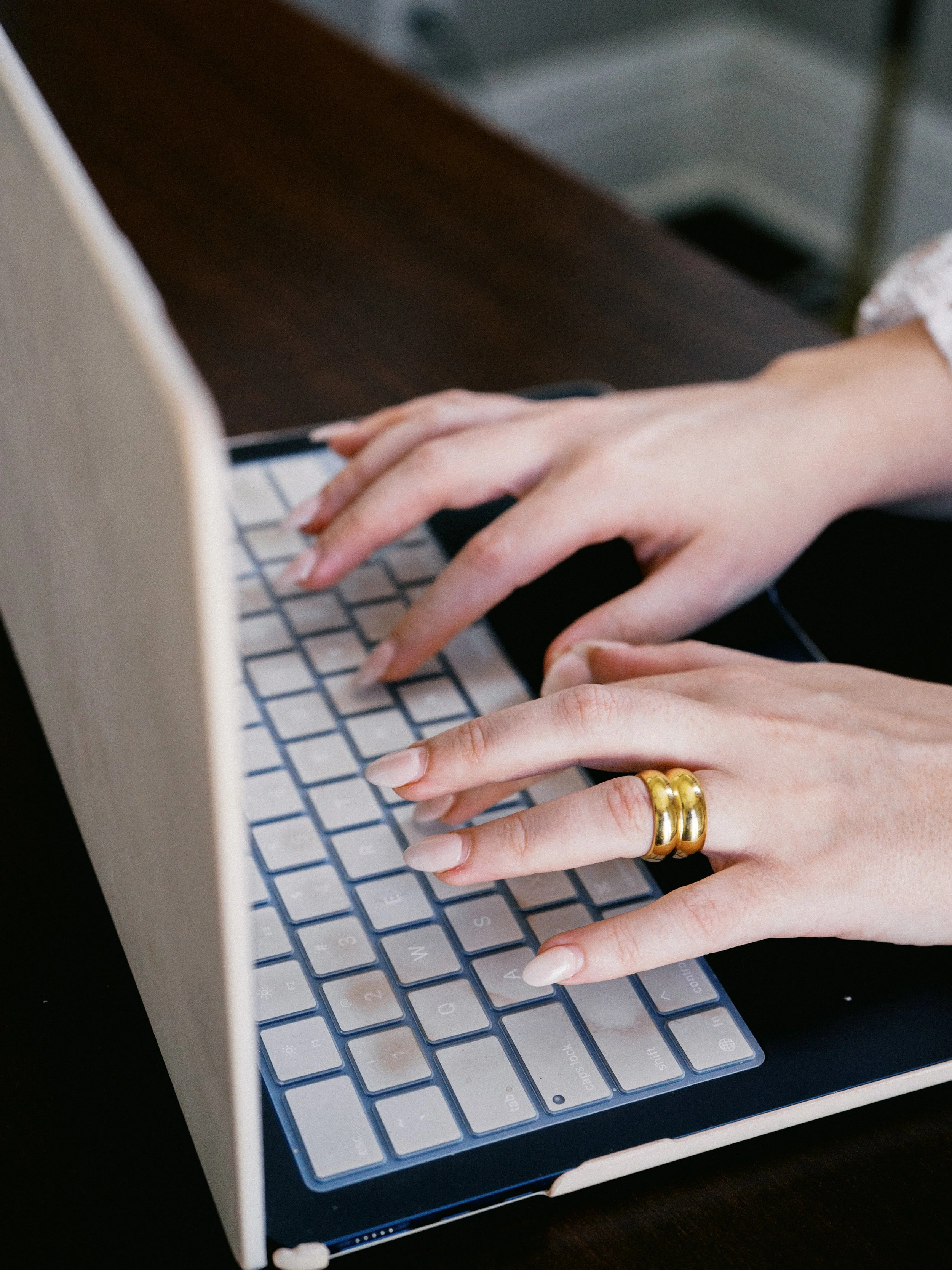 Close-up of hands typing on a light-colored keyboard with a dark wooden surface underneath.