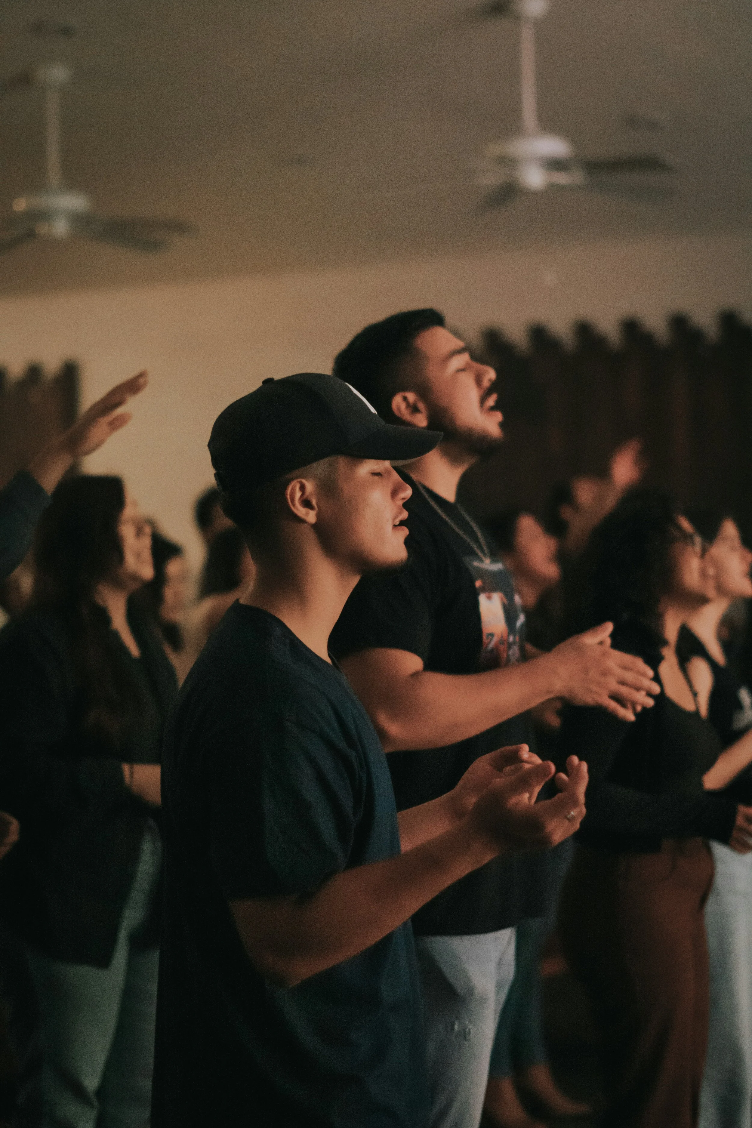 Group of people with eyes closed, praying, and raising their hands in a religious gathering.