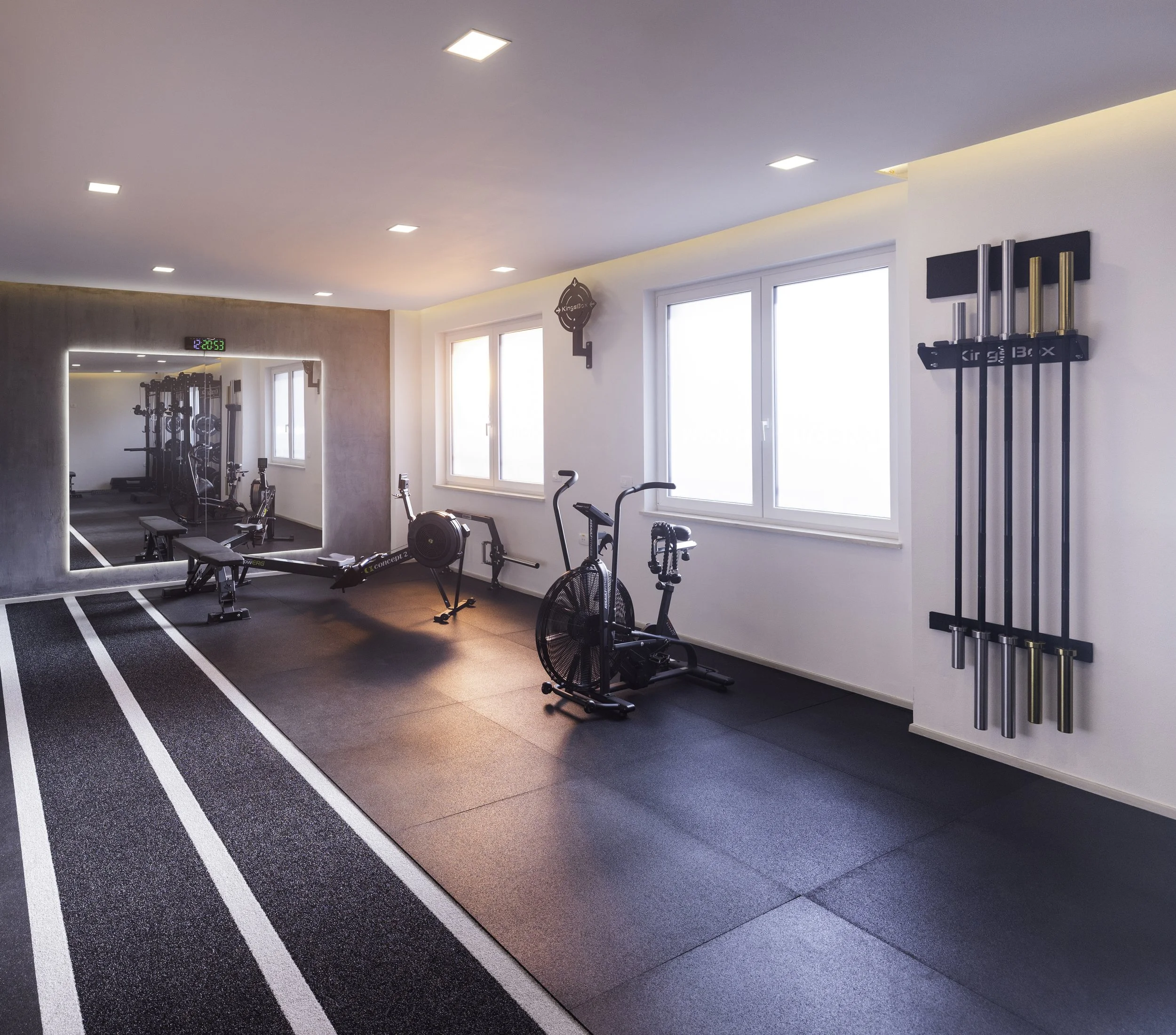 Inside view of a gym with workout equipment, a mirror, windows, and workout tracks on the floor.