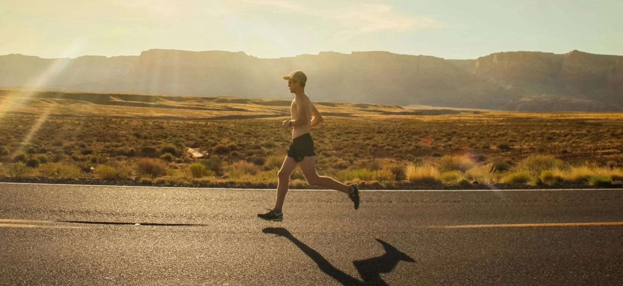 A man runs on a road in a desert landscape during sunset, with mountains in the background.