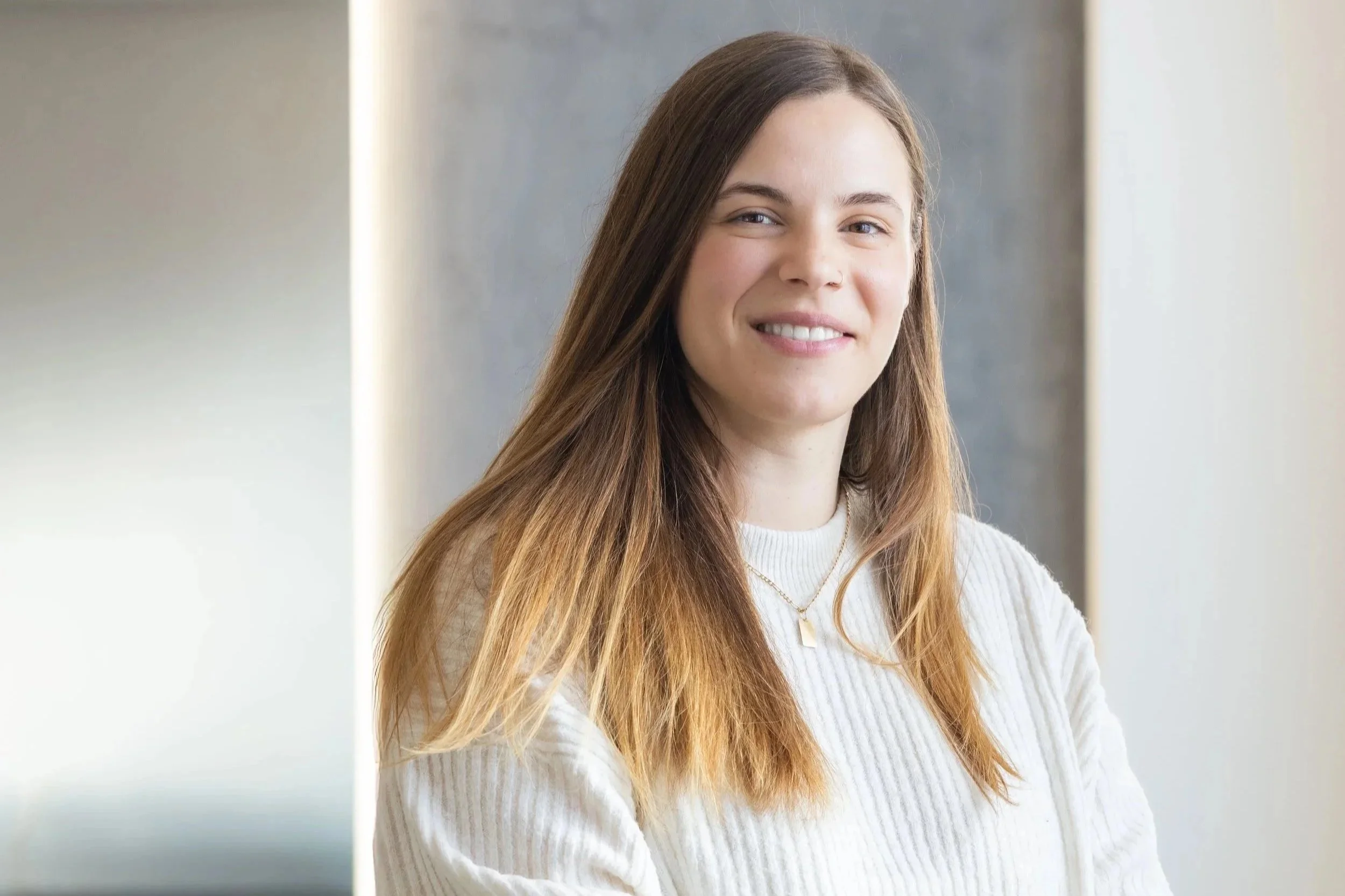 A young man sitting on a bench in a minimalistic room, wearing a gray polo shirt and cream-colored pants, casting a prominent shadow on the wall.
