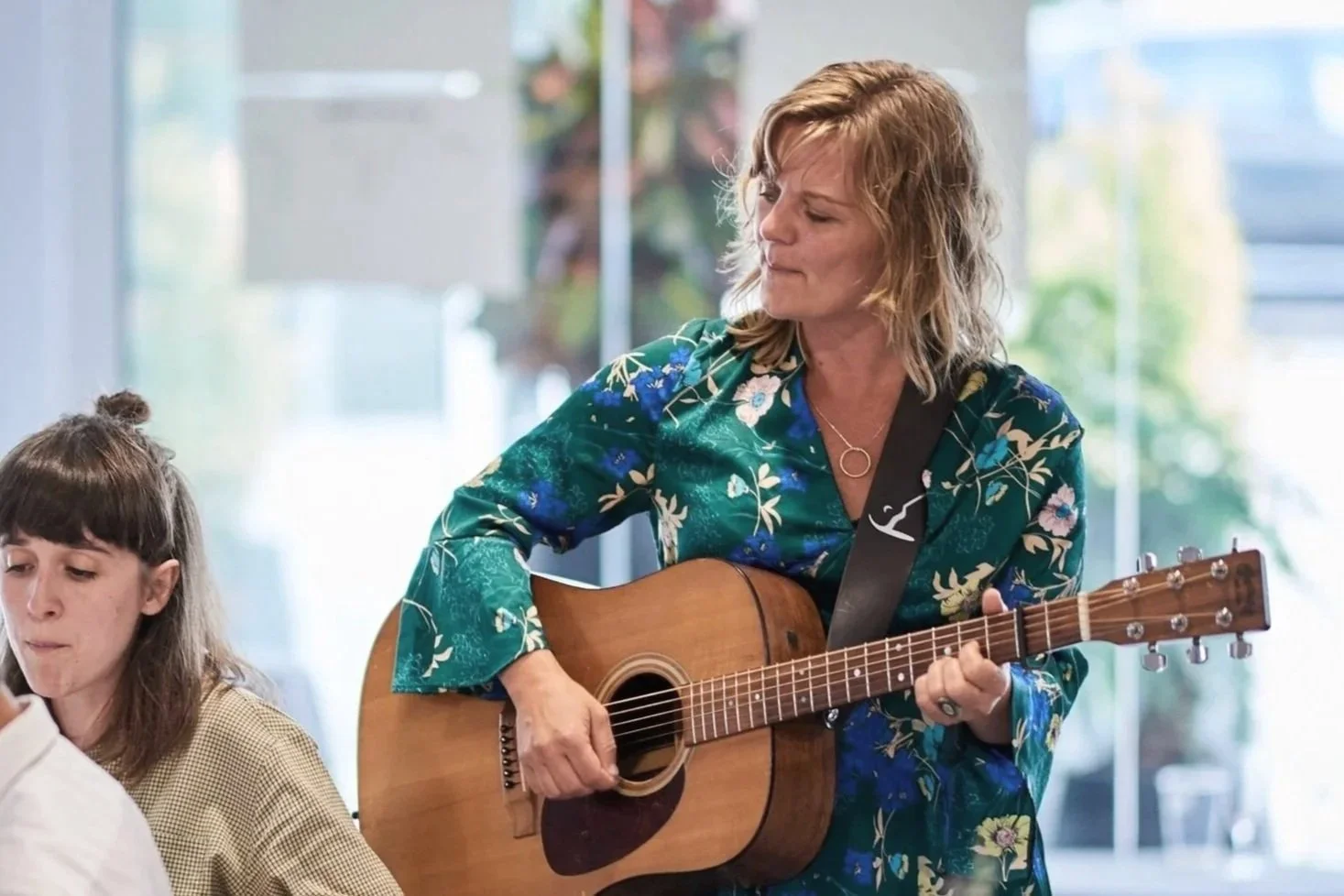 En kvinde spiller guitar, mens en ung pige sidder ved siden af hende.