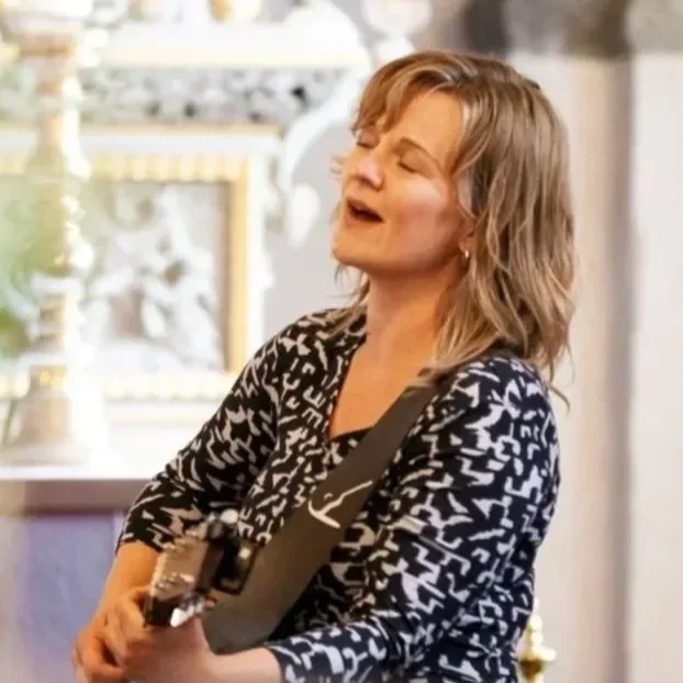 En kvinde der synger og spiller guitar i et indendørs lokale.