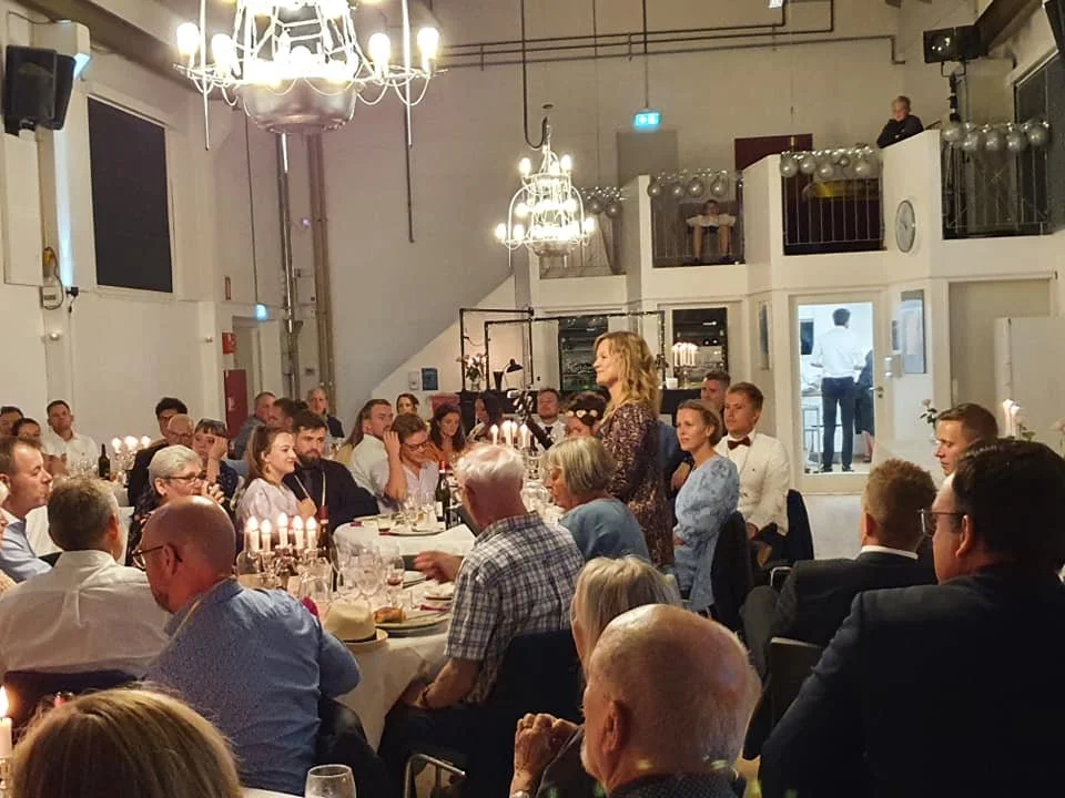 Mennesker til festmiddag, med tændte stearinlys og dekorationer, i en stor, veludstyret spisestue med en kvinde, der står op foran bordet.