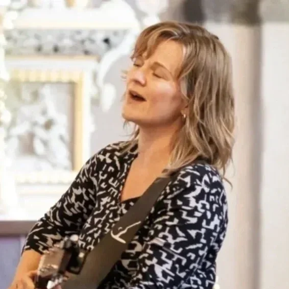 Kvinde spiller guitar og synger med lukket øjne i et lyst rum.