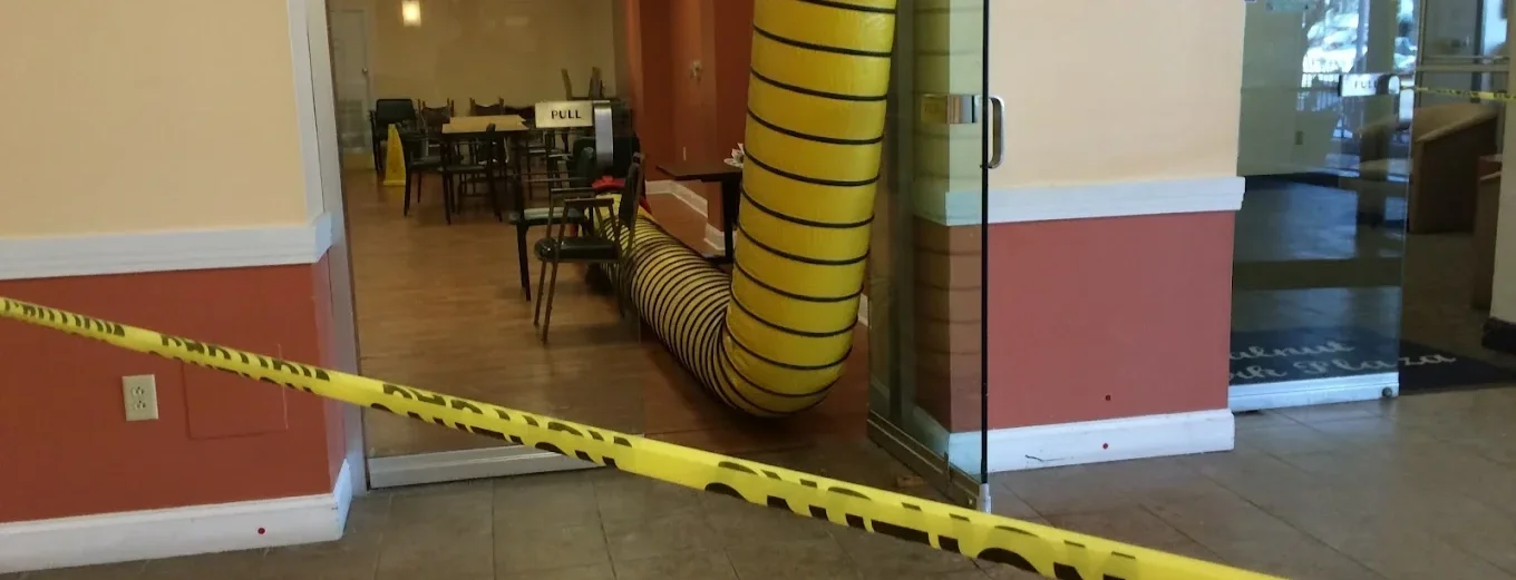 A yellow and black striped flexible ventilation duct inside a restaurant or cafe, with a caution tape across the entrance that says 'Caution.'