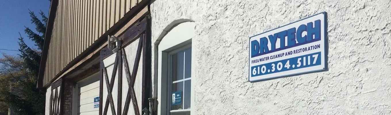 Sign for DRYTECH fire and water cleanup and restoration business on white exterior wall of building