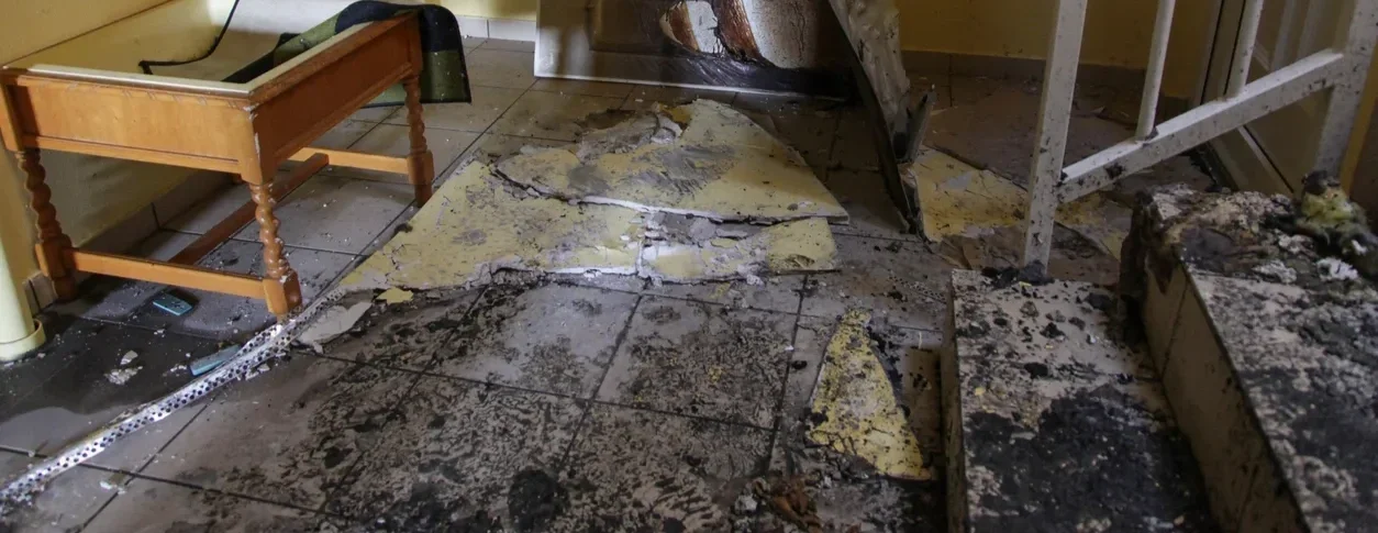 Flooded room with damaged tiles, debris, and burnt furniture.
