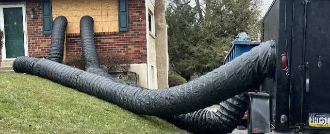 Large black vacuum hoses extended from a house to a large black truck parked outside.