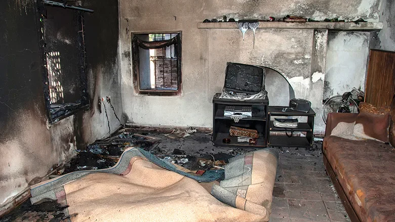 Living room with burnt furniture and damaged walls, showing signs of fire damage.