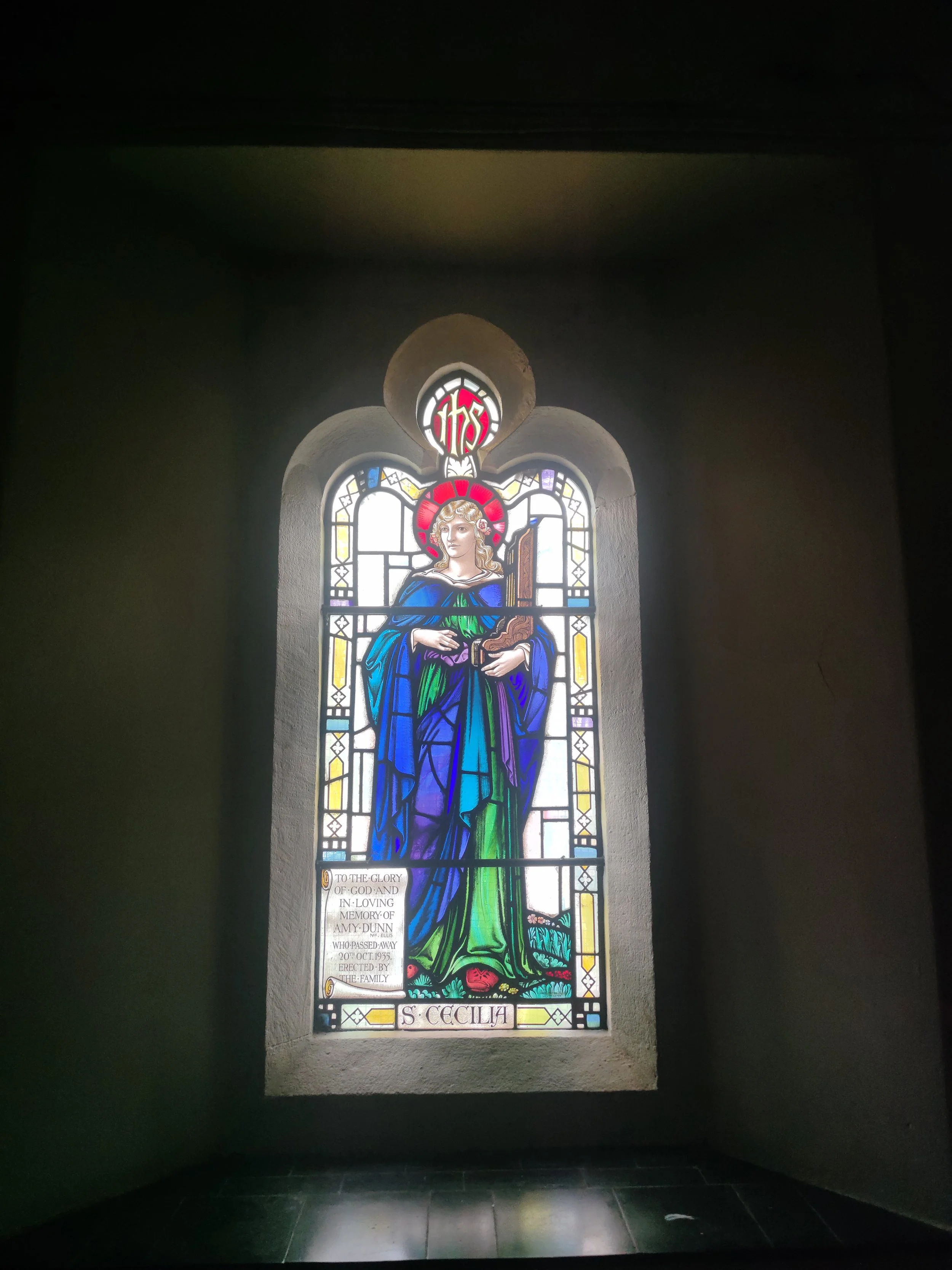 Penge Congregational Church. Colorful stained glass window depicting Saint Cecilia holding a musical instrument, with a decorative border and a plaque at the bottom reading 'S. CECILIA: patron of music. 