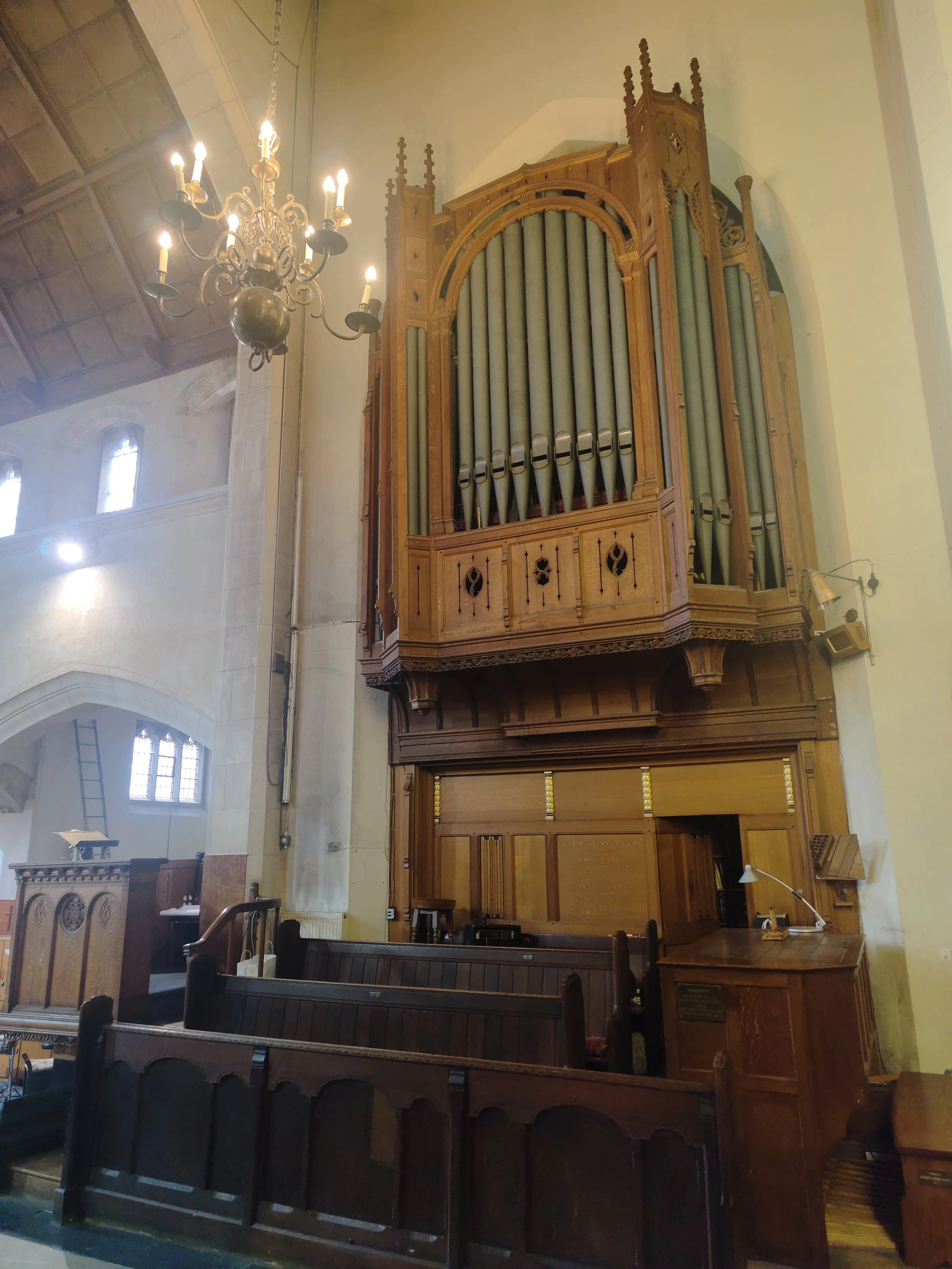 Penge Congregational Church. A large pipe organ in a church with wooden casing, surrounded by wooden pews and a chandelier hanging from the ceiling.
