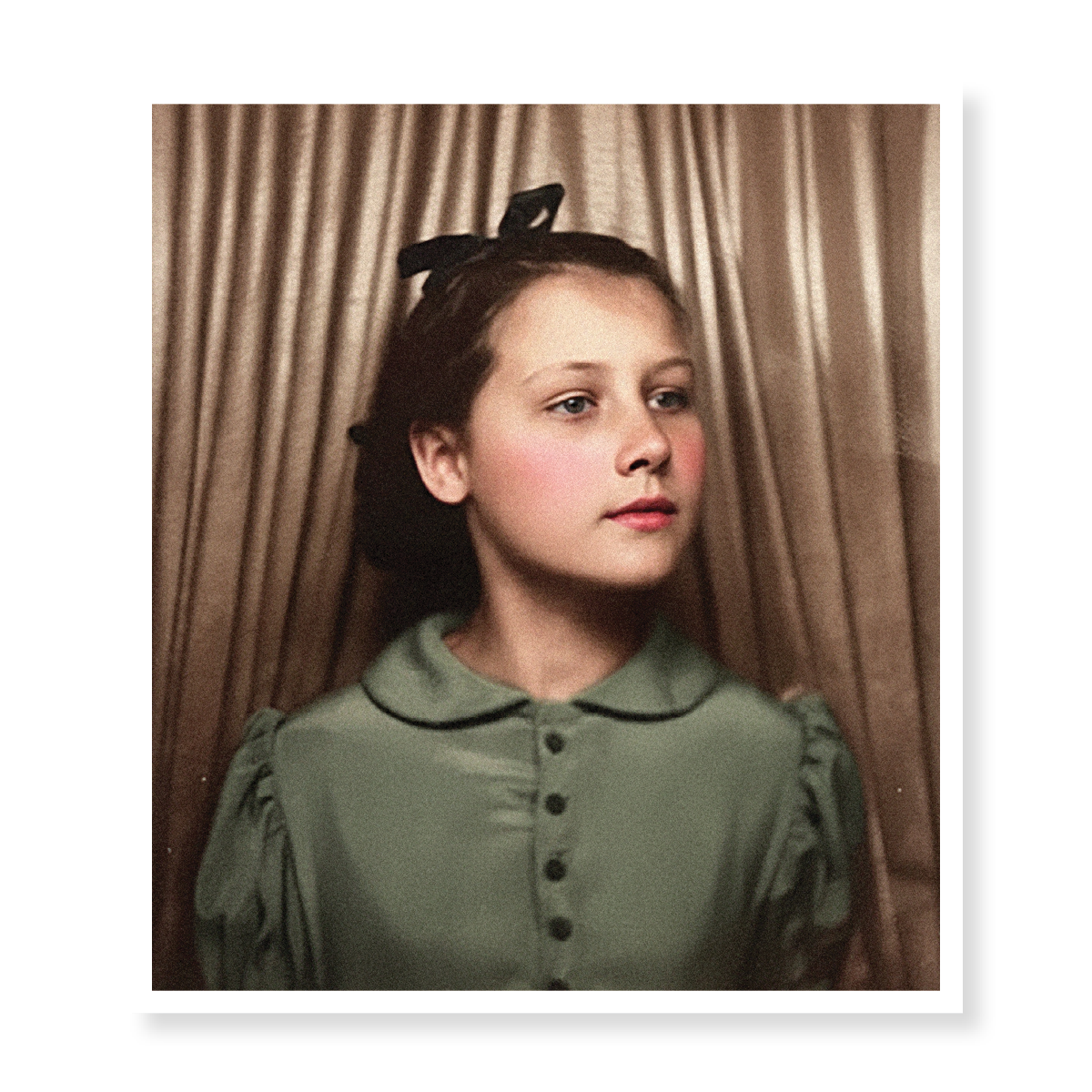 A young girl with light brown hair styled with a black bow, wearing a green blouse with a rounded collar, standing in front of a beige curtain.
