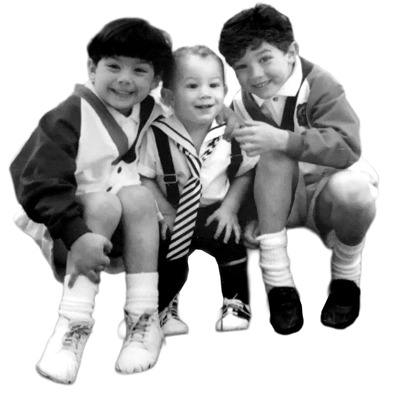 Three young children sitting together, dressed in school uniforms, smiling for the camera.