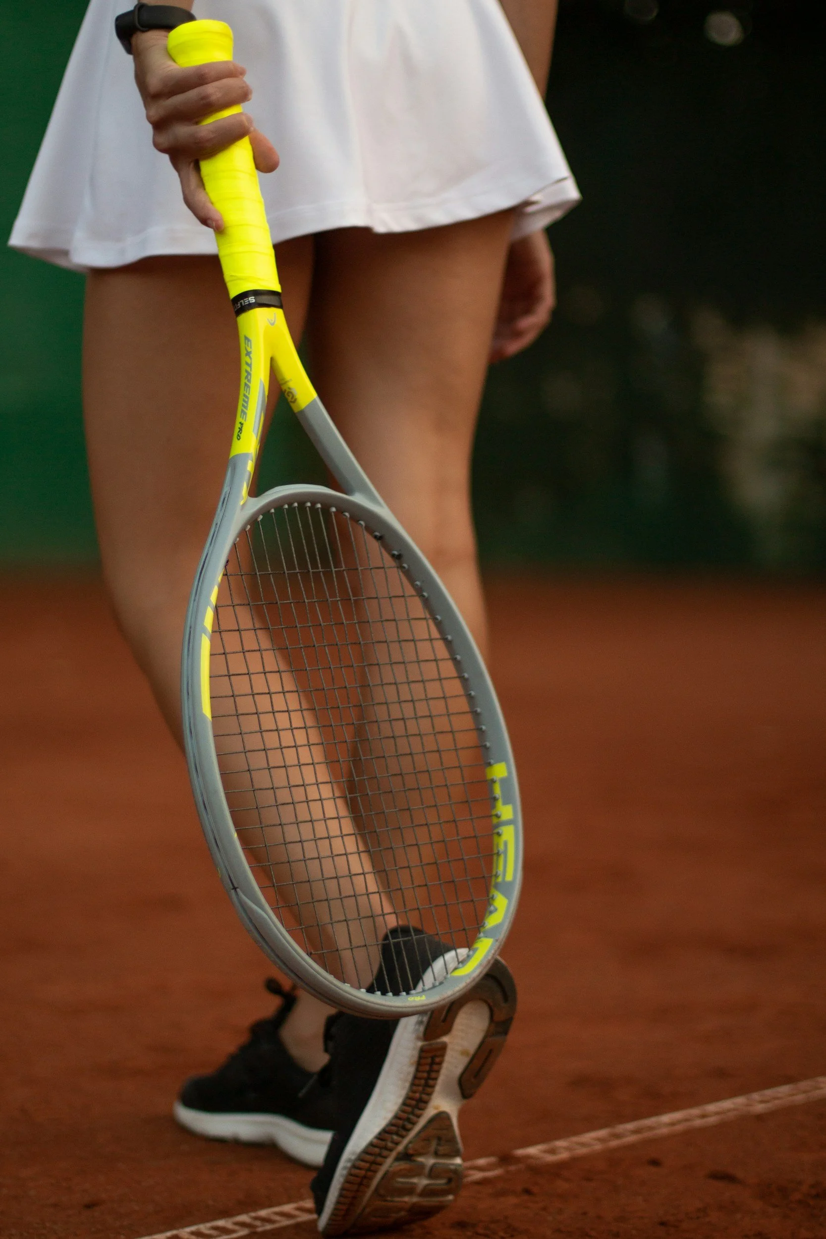 Close-up of a female tennis player holding a yellow and gray tennis racket on a clay court.